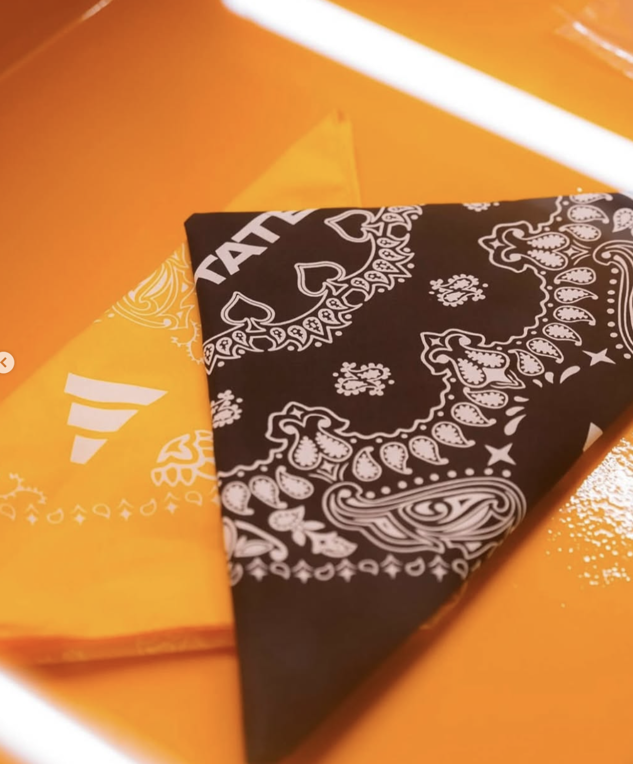 Two folded bandanas, one orange and one black, with paisley patterns on a shiny surface.