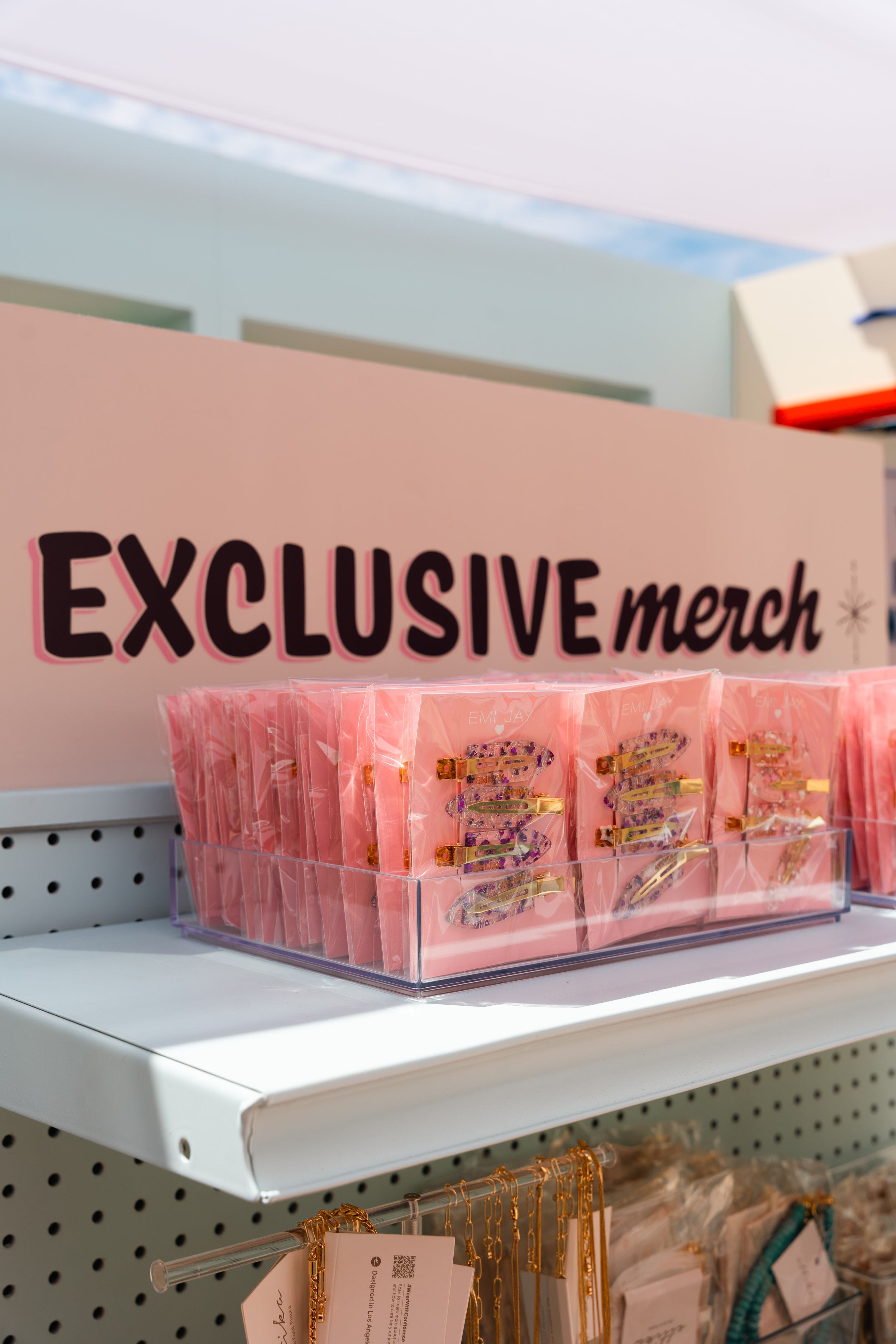 Shelf displaying exclusive merchandise with hair clips in pink packaging and necklaces below it in a store.