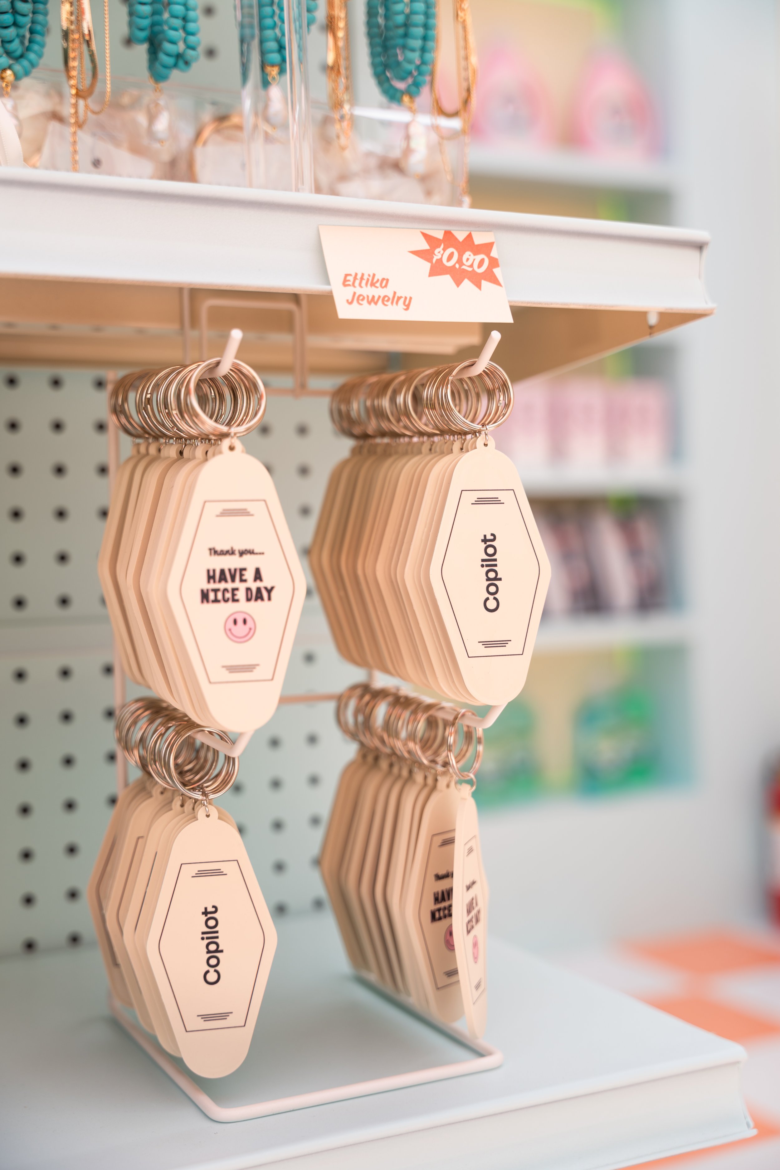 Keychains labeled "Copilot" and "Have a Nice Day" displayed on a rack with a sign "Ettika Jewelry $0.00" above, in a retail setting.