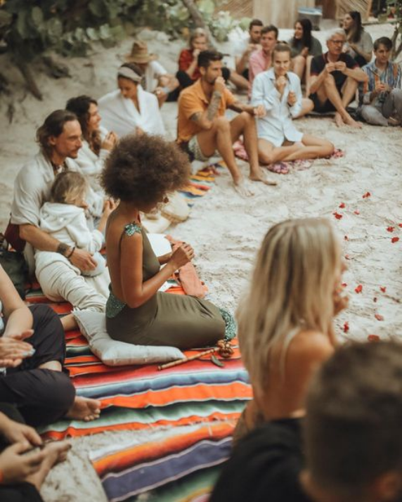 People gathered on a beach sitting on colorful blankets participating in a cacao ceremony in Tulum