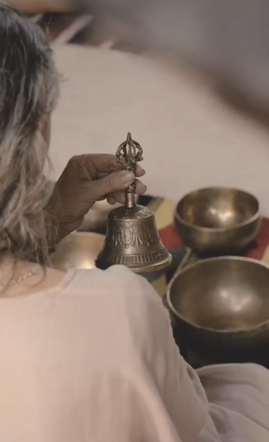 A person holding a small ornate bell with a handle during a sound healing