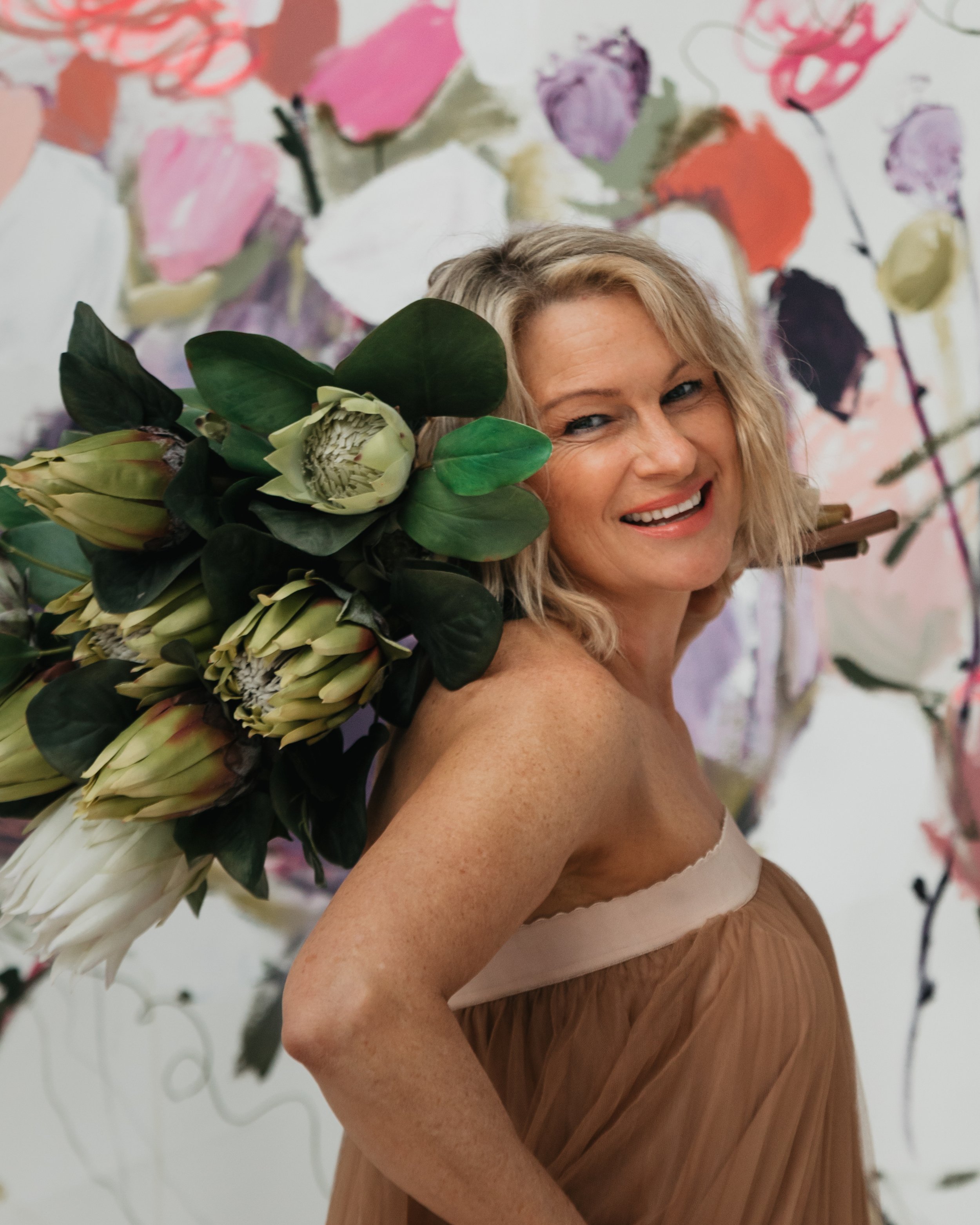 me standing in front of m,y artwork, holding a bunch of flowers over my shoulder