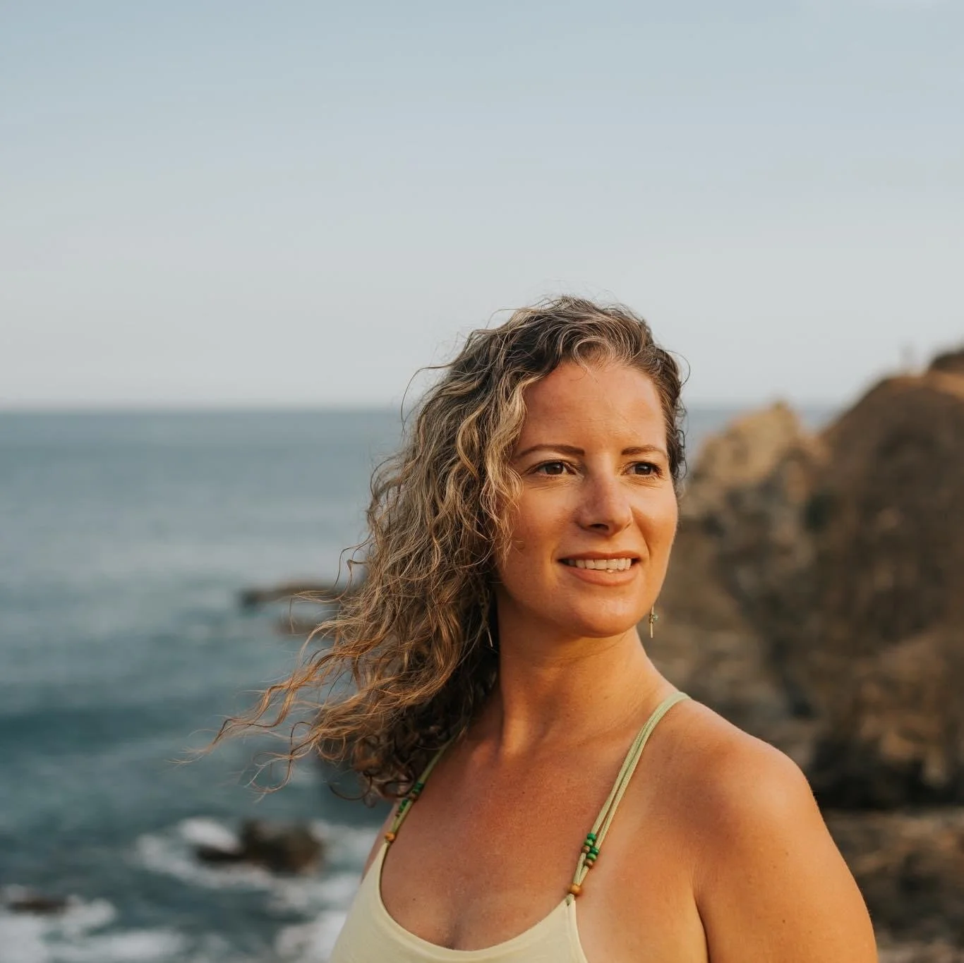 Woman with wavy blonde hair looks back over the ocean.