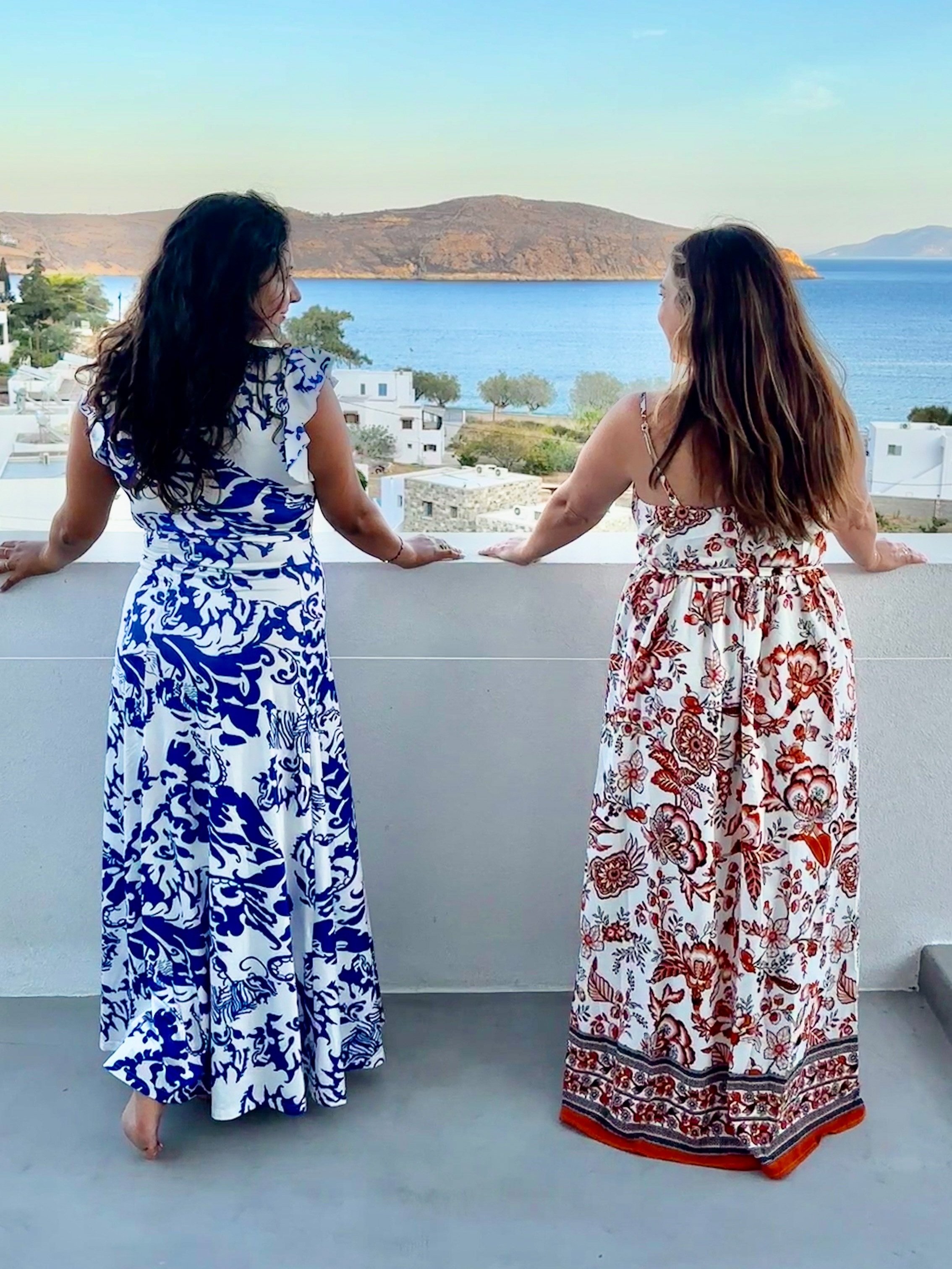 Two women in dresses taking in the Grecian views on the Nostos balcony.