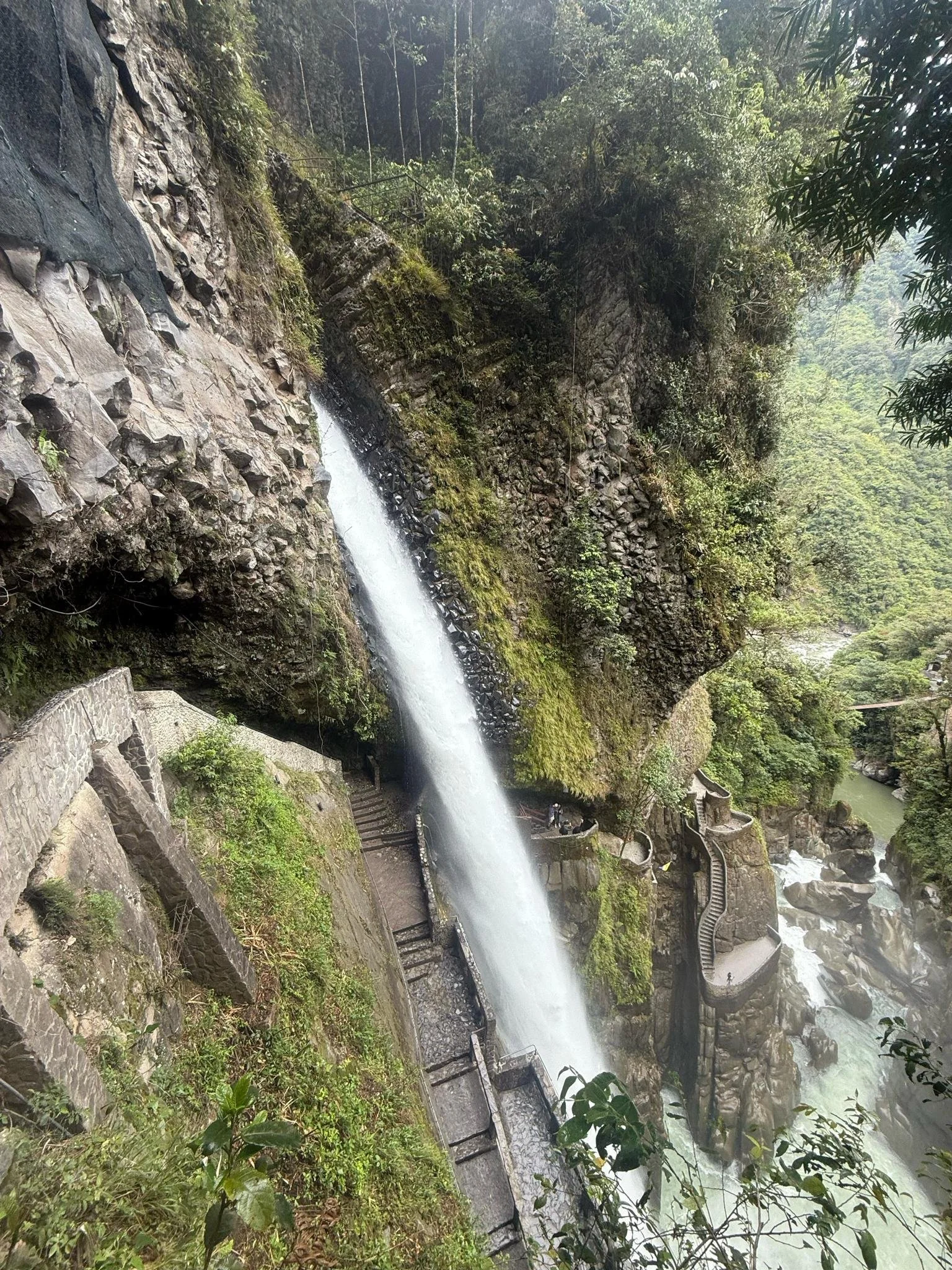 Aerial view of Pailon del Diablo waterfall cascading through moss-covered rock canyon with wooden walkways and stairs visible along the cliff face