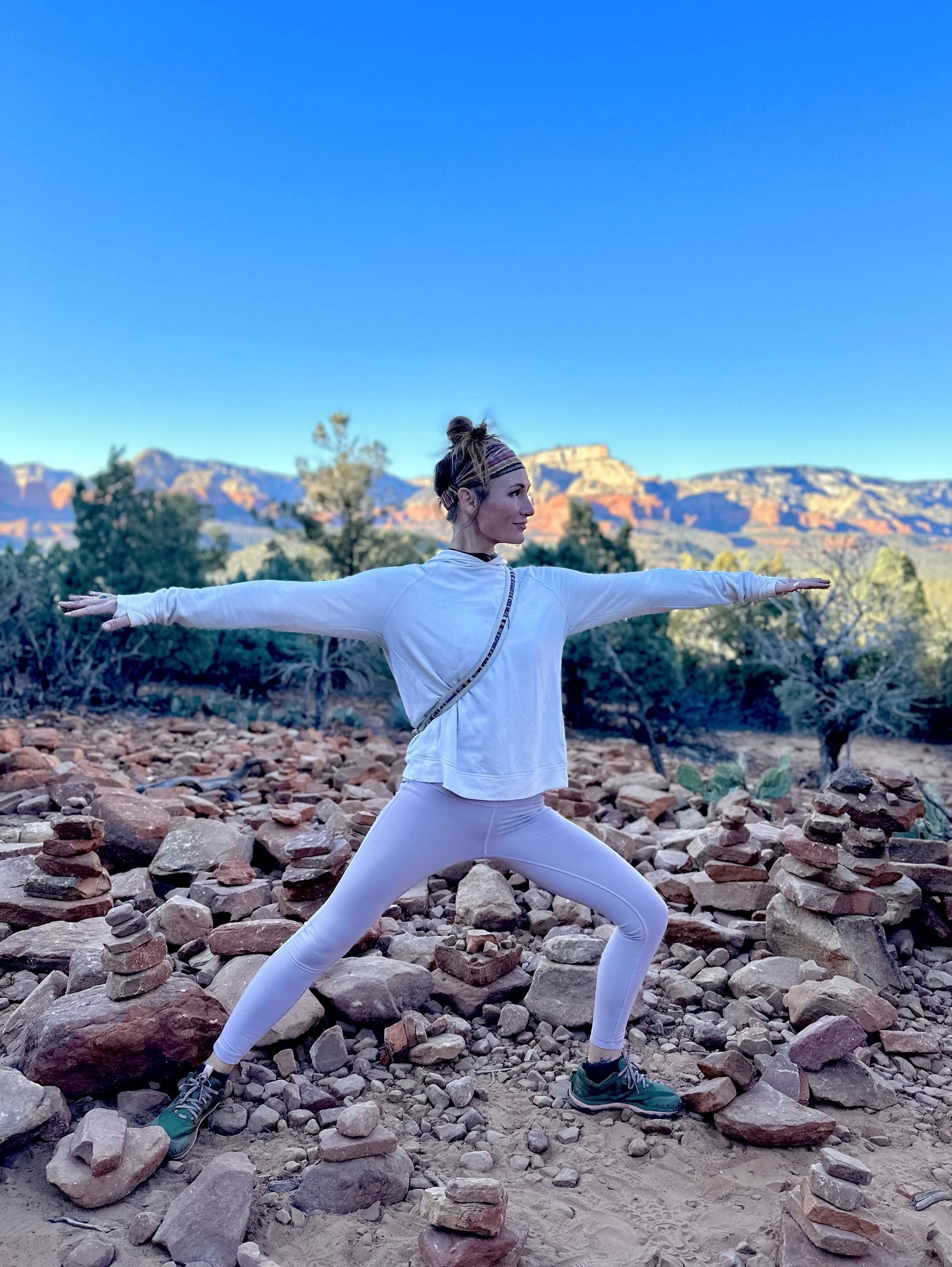 A woman practicing yoga outdoors among rocks with a mountain landscape in the background