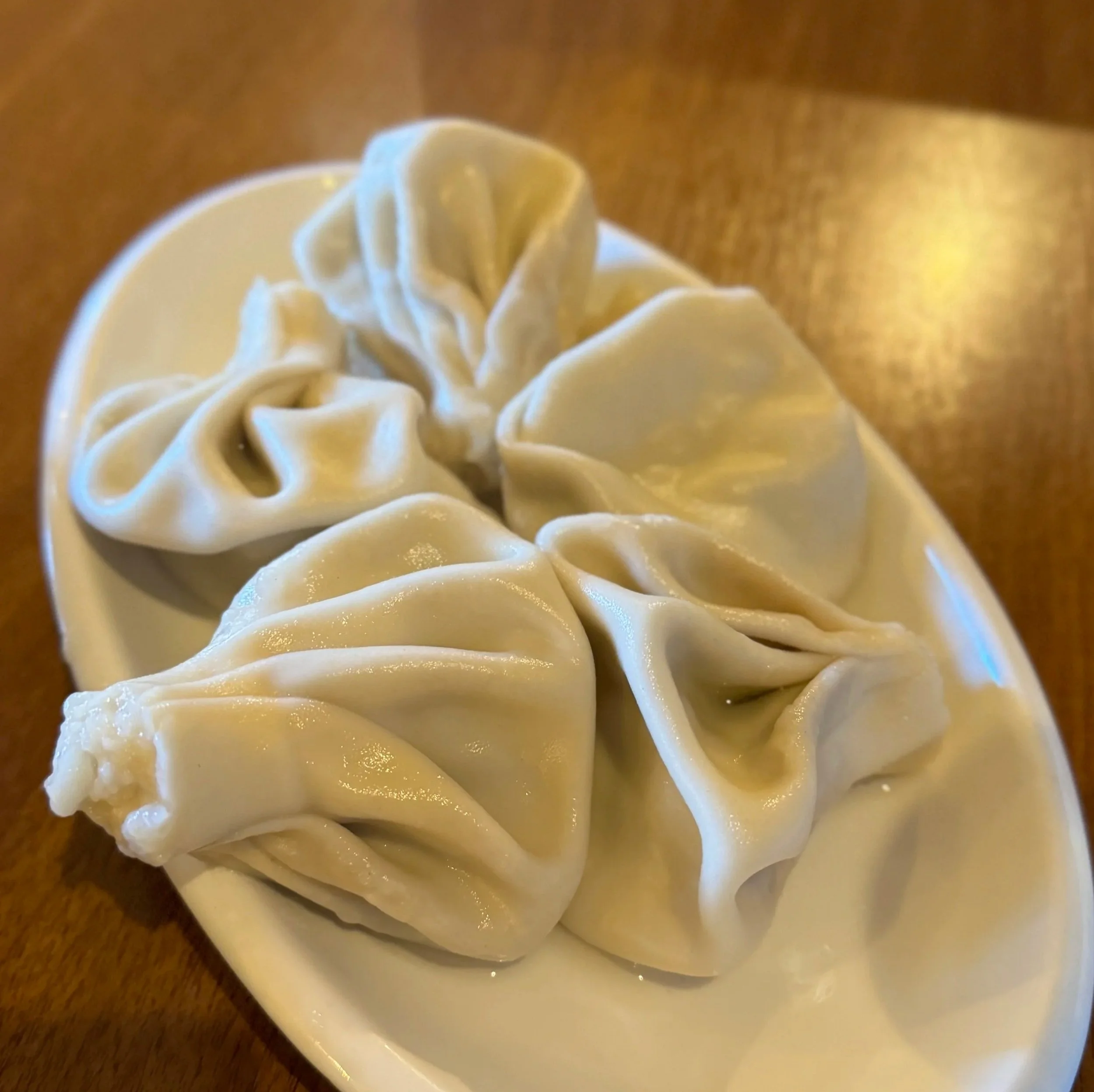 Three Georgian khinkali dumplings on a white plate, showing their characteristic pleated tops and pale dough, served on a wooden table