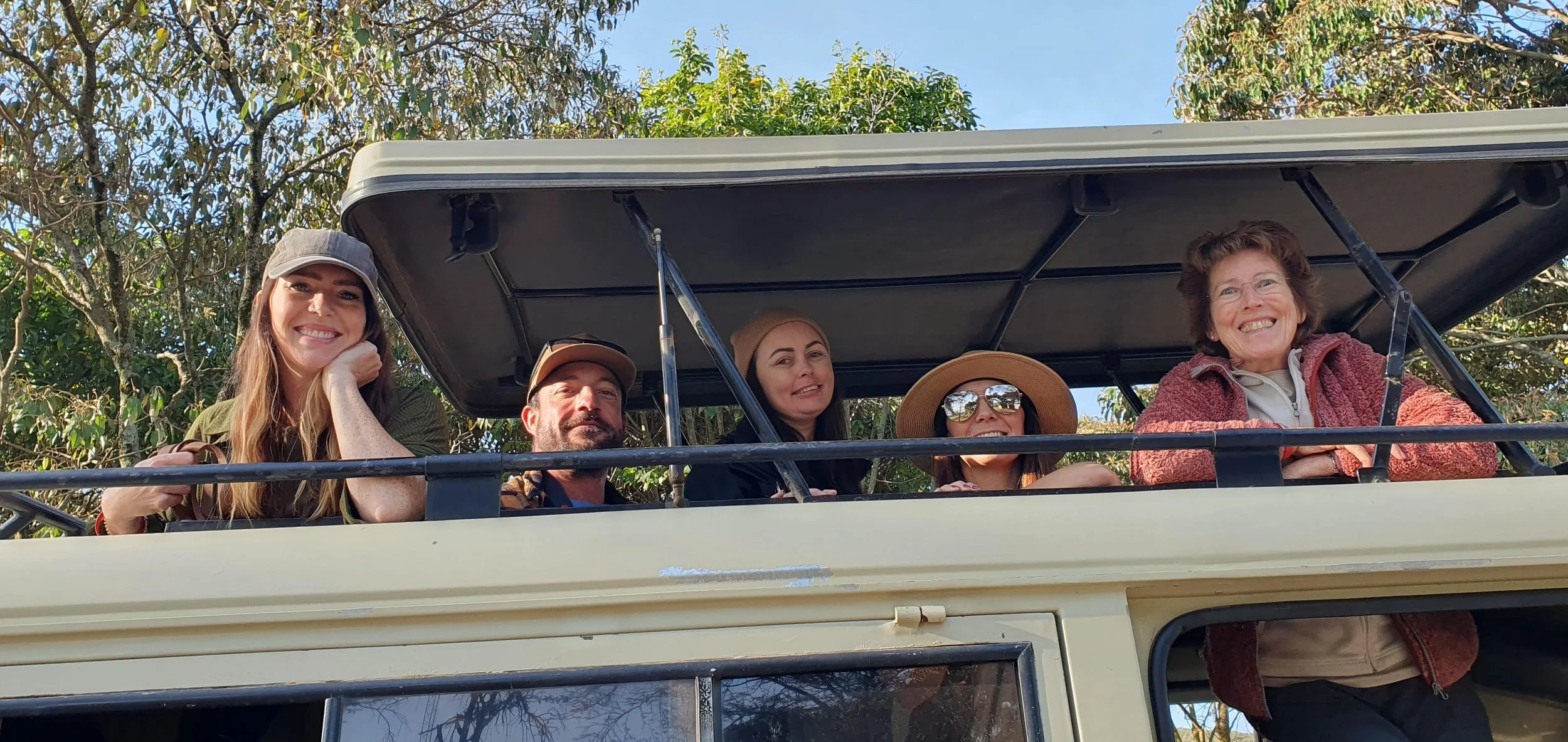 Travelers on safari vehicle in Kenya wildlife reserve during group adventure tour with pop-up roof