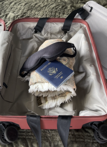 Open carry-on suitcase with a rolled scarf, black sleep mask, and U.S. passport packed inside.