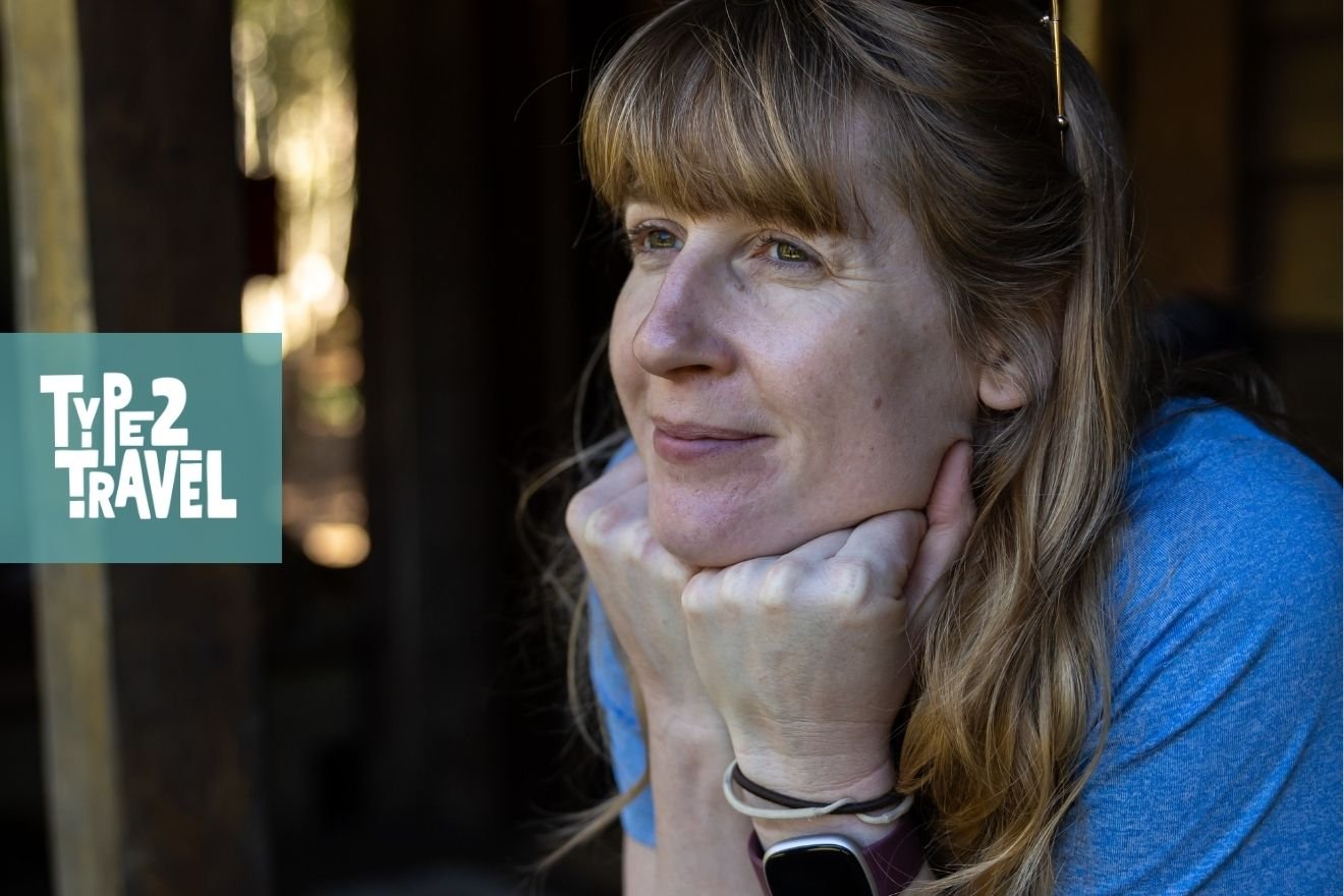 Steph Dyson in a thoughtful pose wearing a blue shirt with long blonde hair, resting her chin on her hand in natural lighting with dark background, Type 2 Travel podcast logo in corner