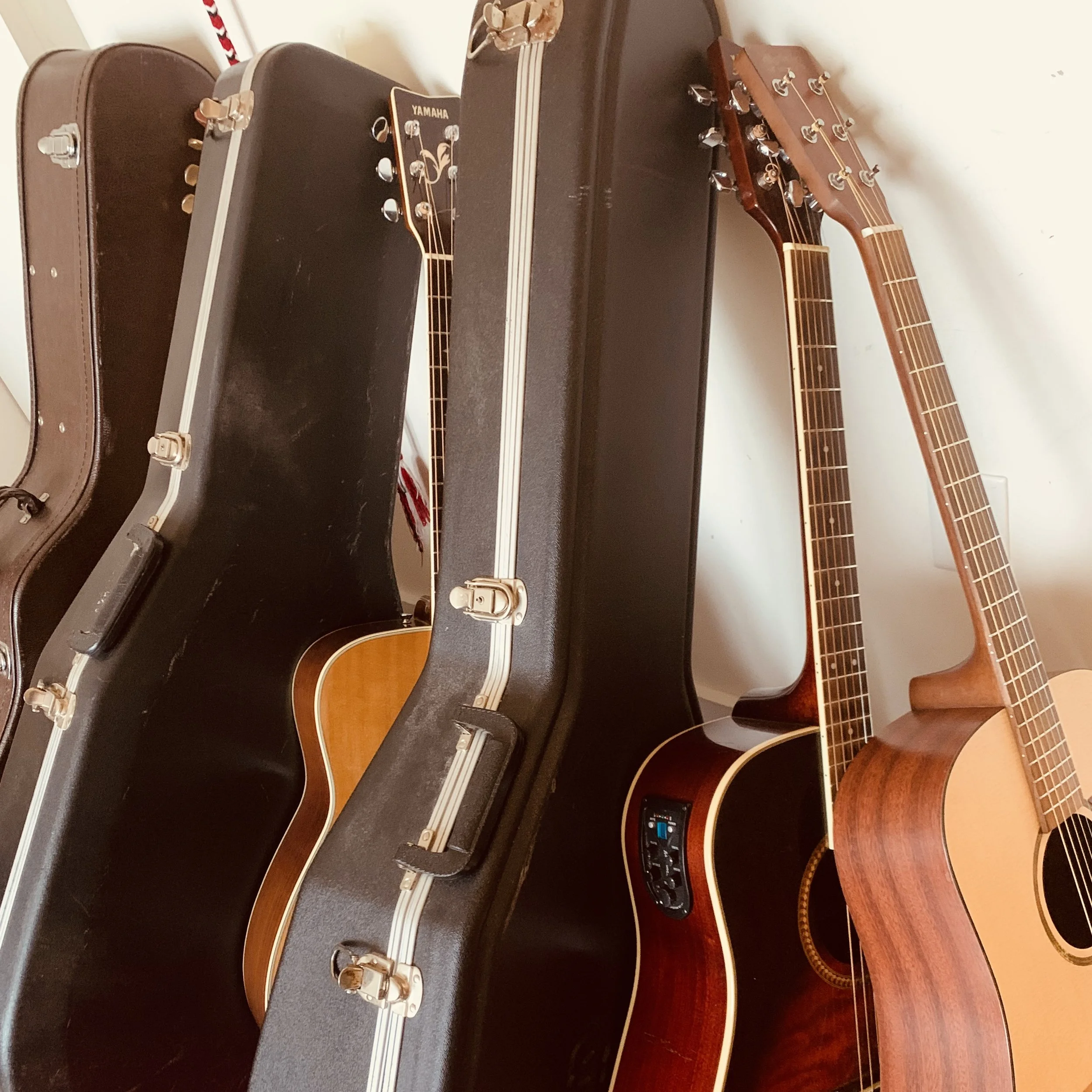 Two acoustic guitars leaning against a wall, with guitar cases behind them.