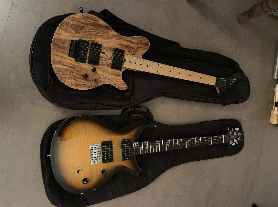 Two electric guitars resting in open black soft cases on a light-colored wooden floor.