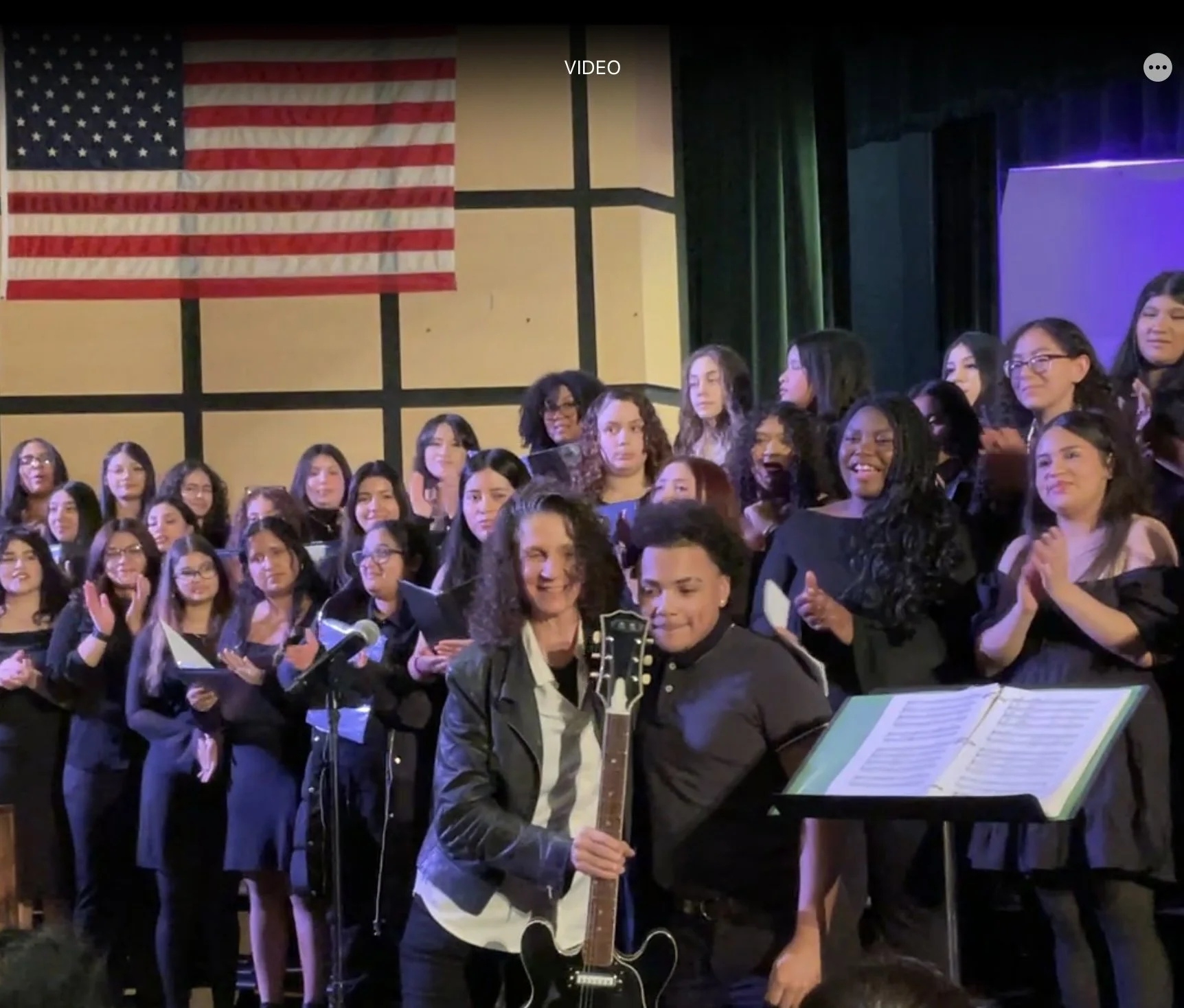 Group of people singing on stage with an American flag hanging in the background.