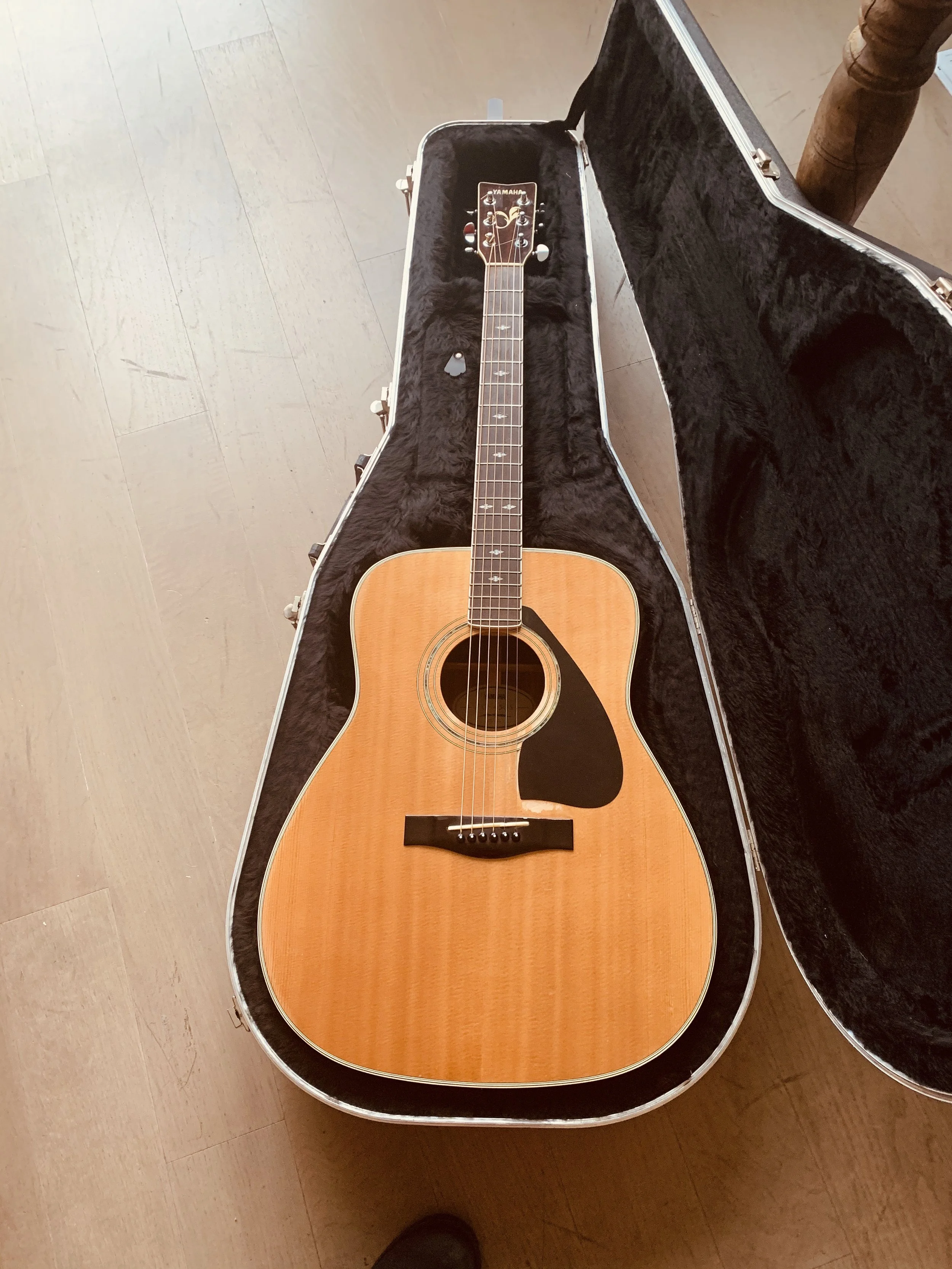 An acoustic guitar resting inside an open black fluffy-lined guitar case on a wooden floor.