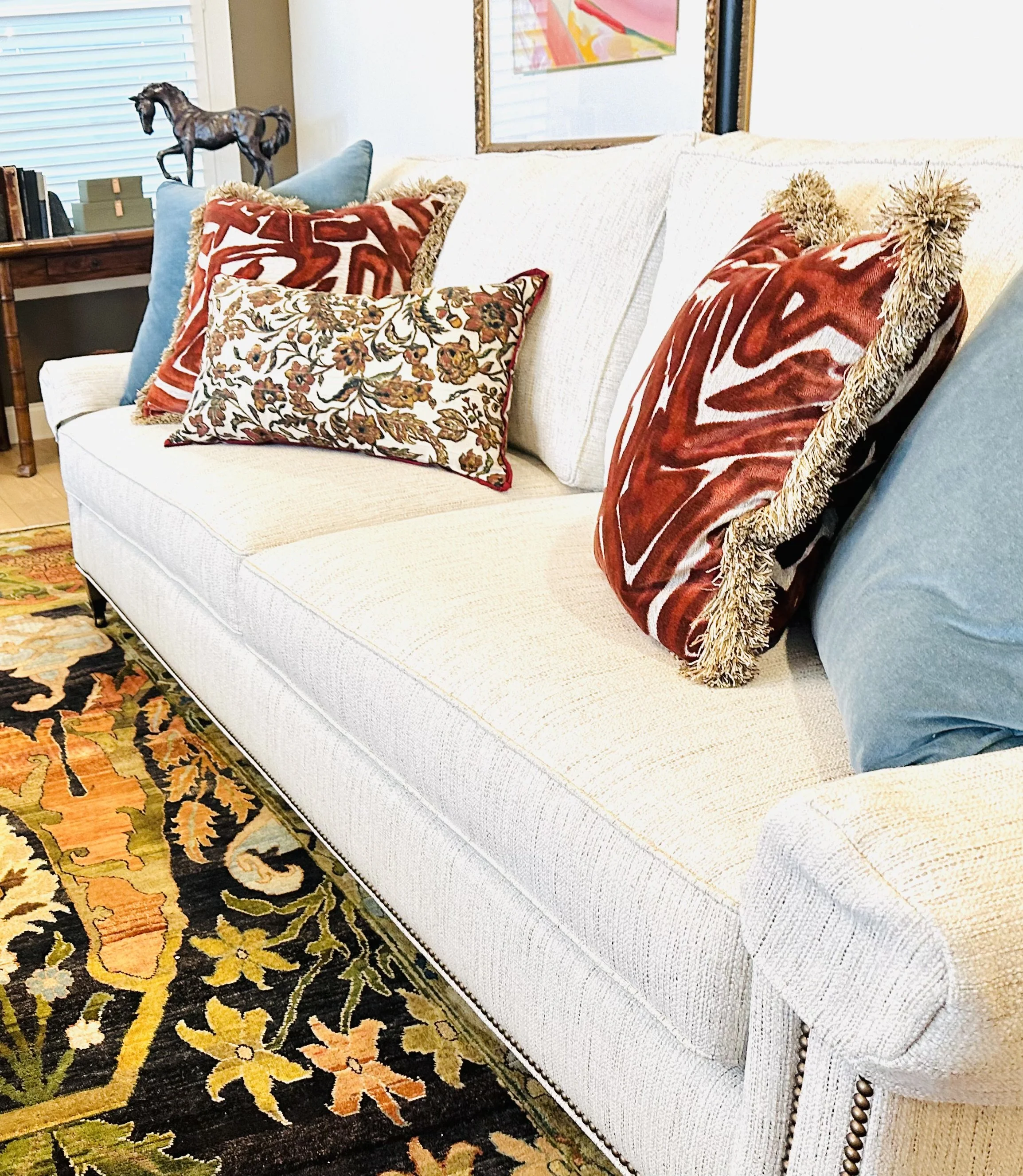 A white sofa with five decorative pillows in various patterns and colors, placed in a living room with a multicolored floral area rug.