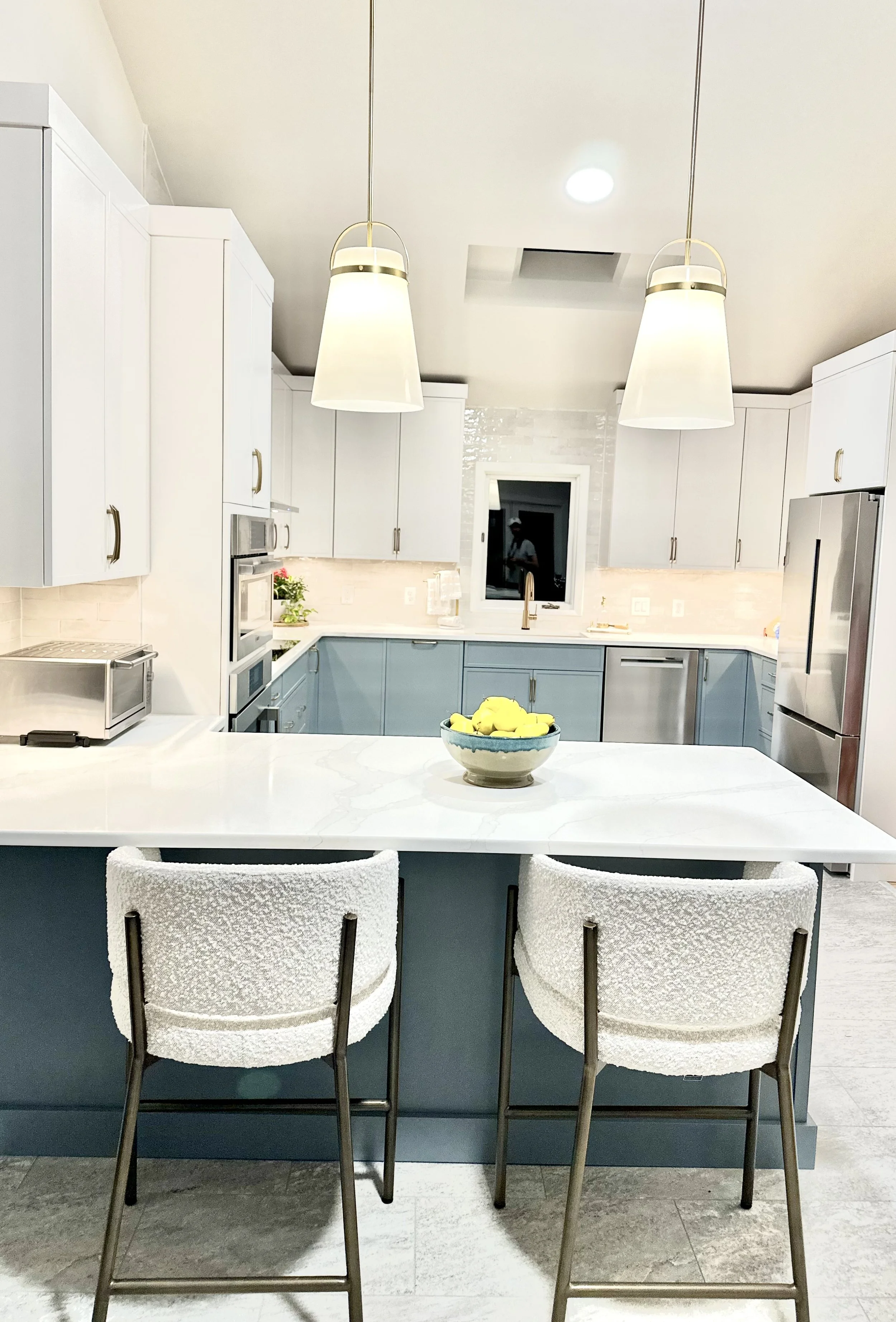 Modern kitchen with white and blue cabinetry, two pendant lights, a bowl of lemons on the island, and two bar stools.