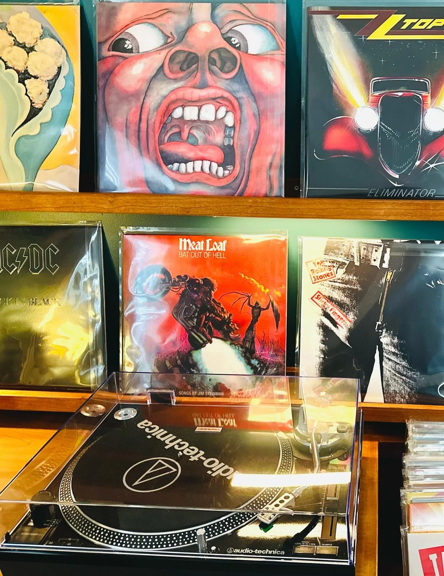 Photo of a record collection with album covers including a landscape with a tree, a screaming face, a vintage race car, AC/DC's "Back in Black," Meat Loaf's "Bat Out of Hell," and a black-and-white punk photo, with a turntable in the foreground.