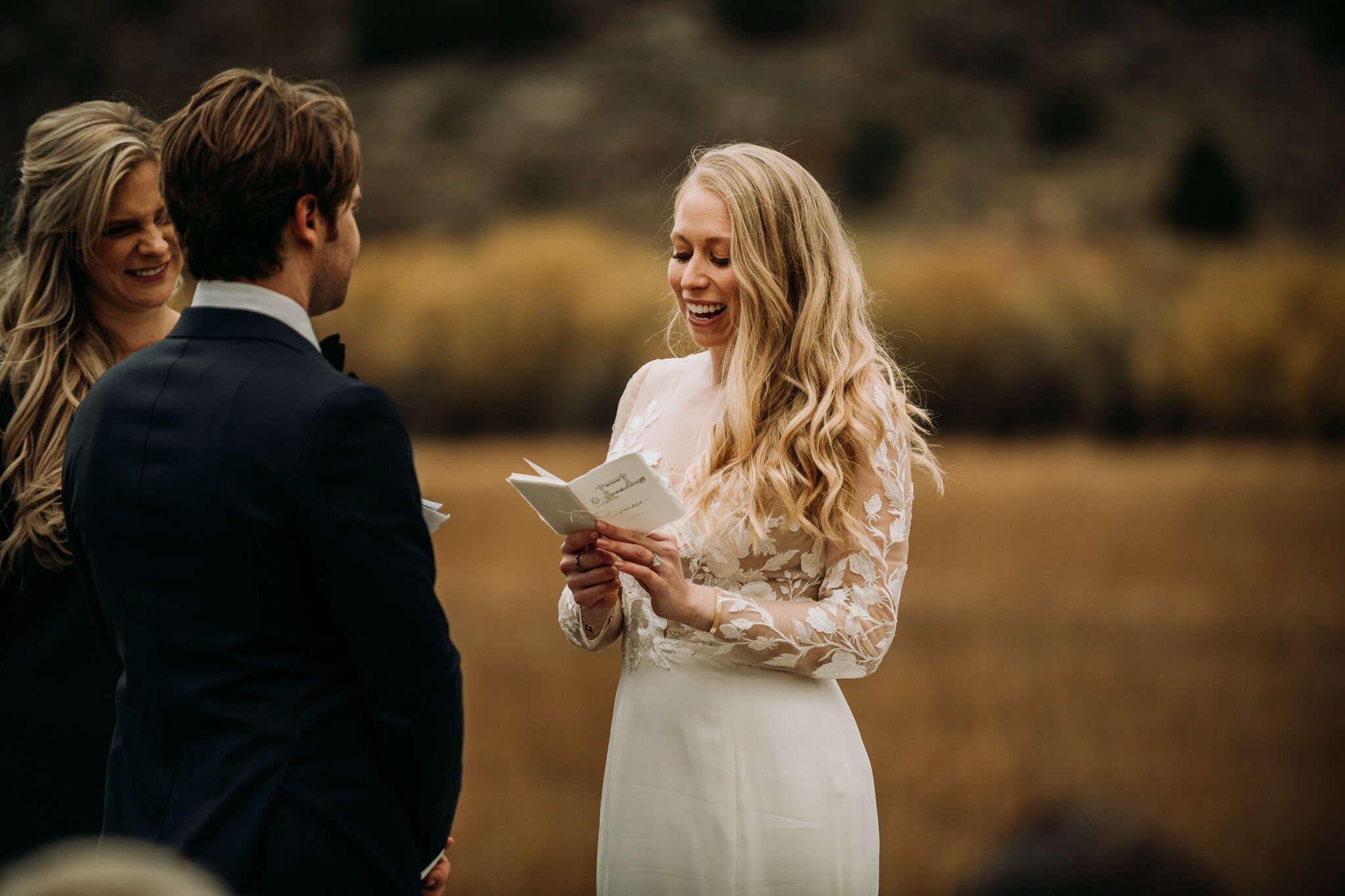 Bride during Fall ceremony at Brush Creek Ranch outdoor wedding reading her vows from a small vow book to groom.