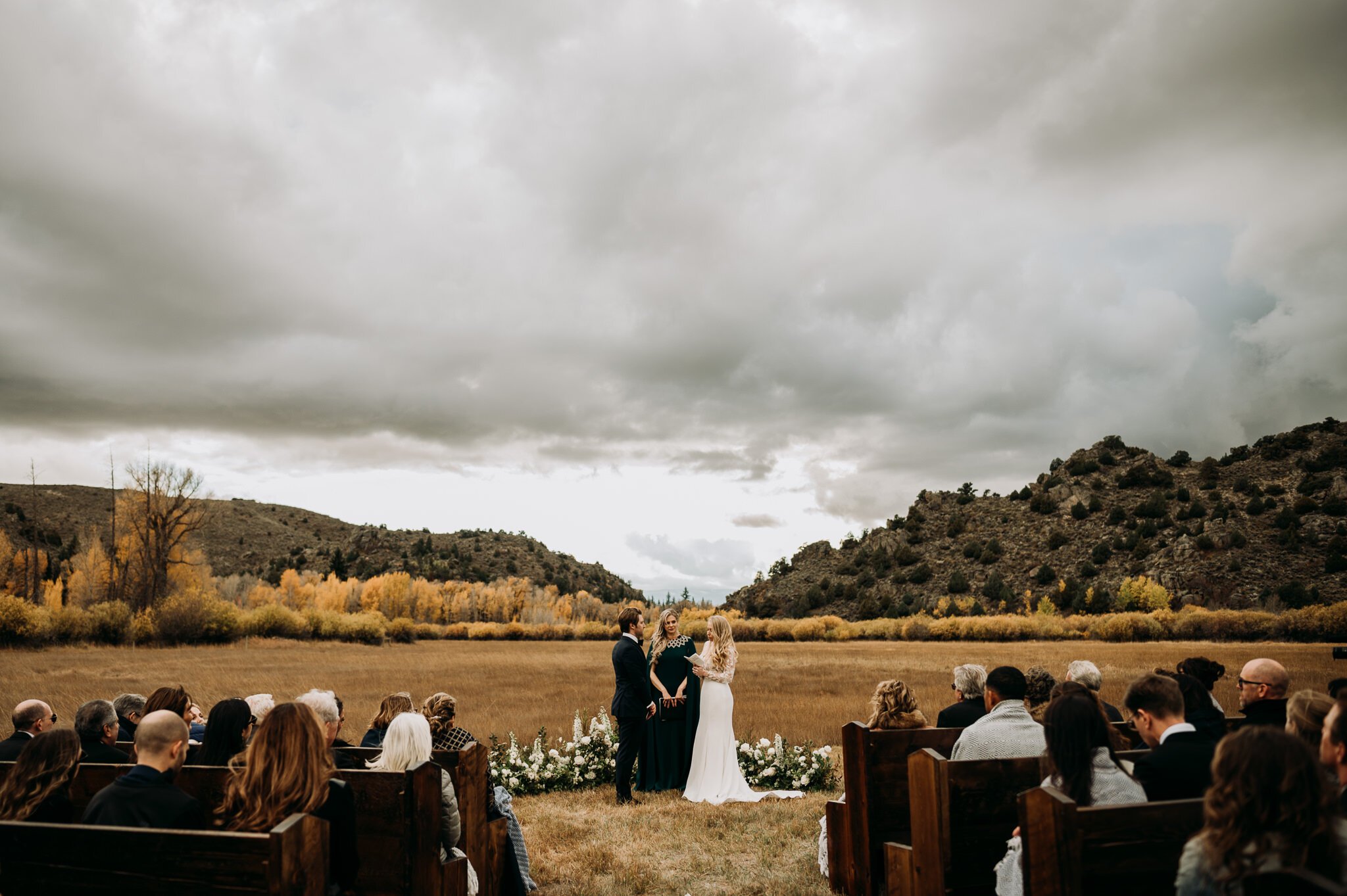 bride and groom at alter in outdoor Fall wedding with guest seated in foreground and the hills and grassy field in back ground, and an awesome big grey sky!