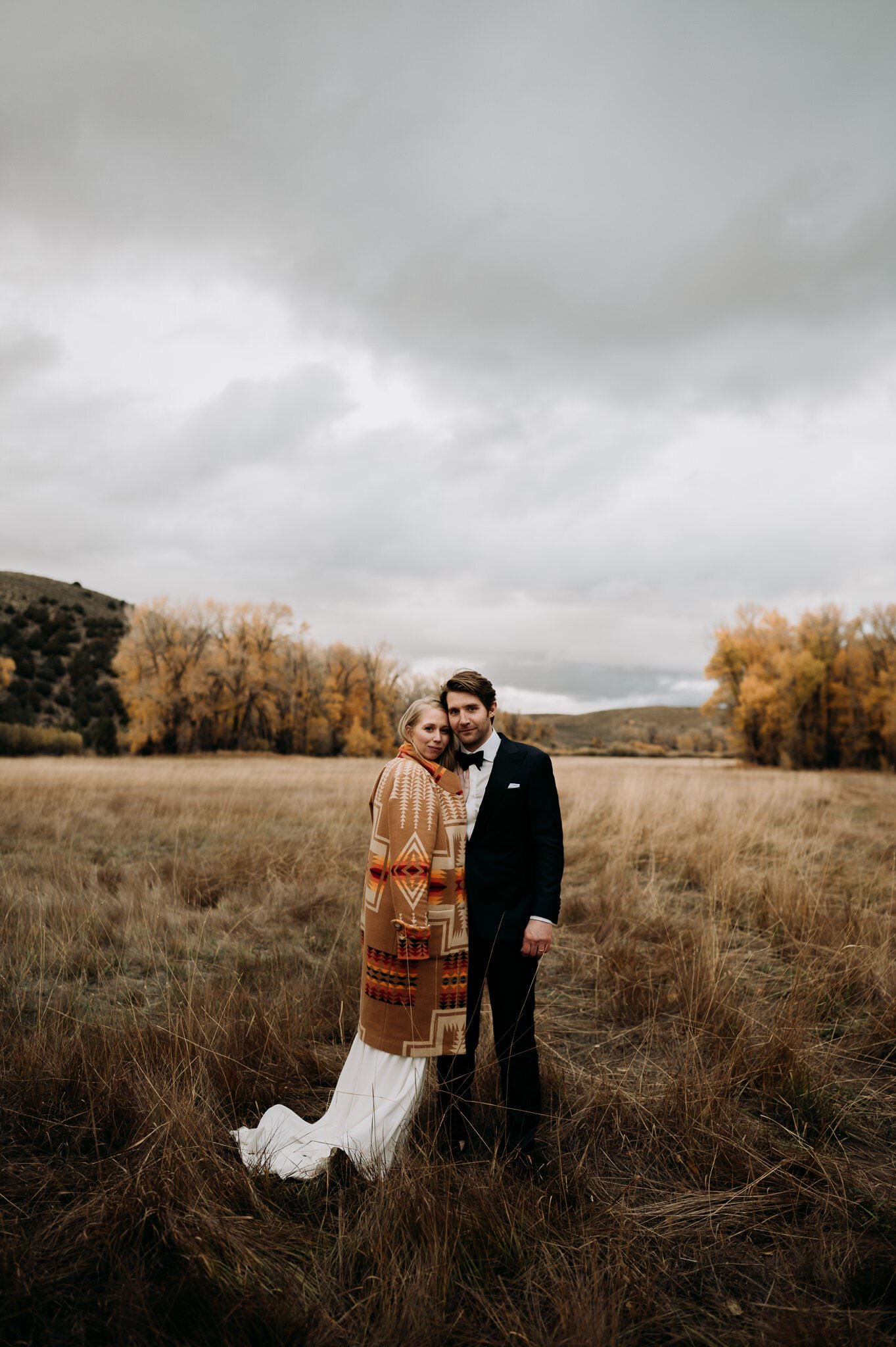 newly married couple in wedding attire standing in a grassy field side by side posing.