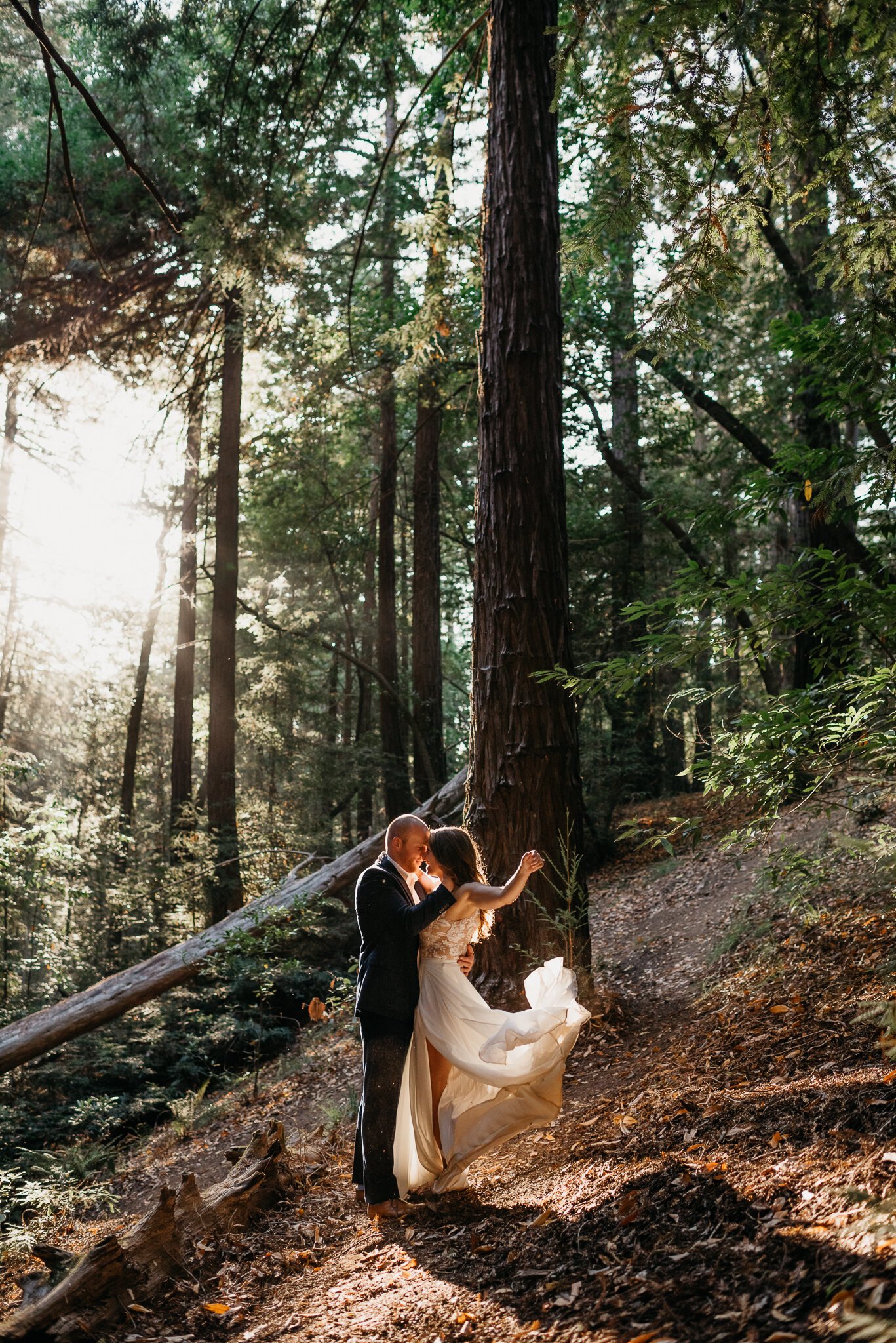 Bride and groom in forest Ventana, Big Sur dancing in the sun peeking through trees