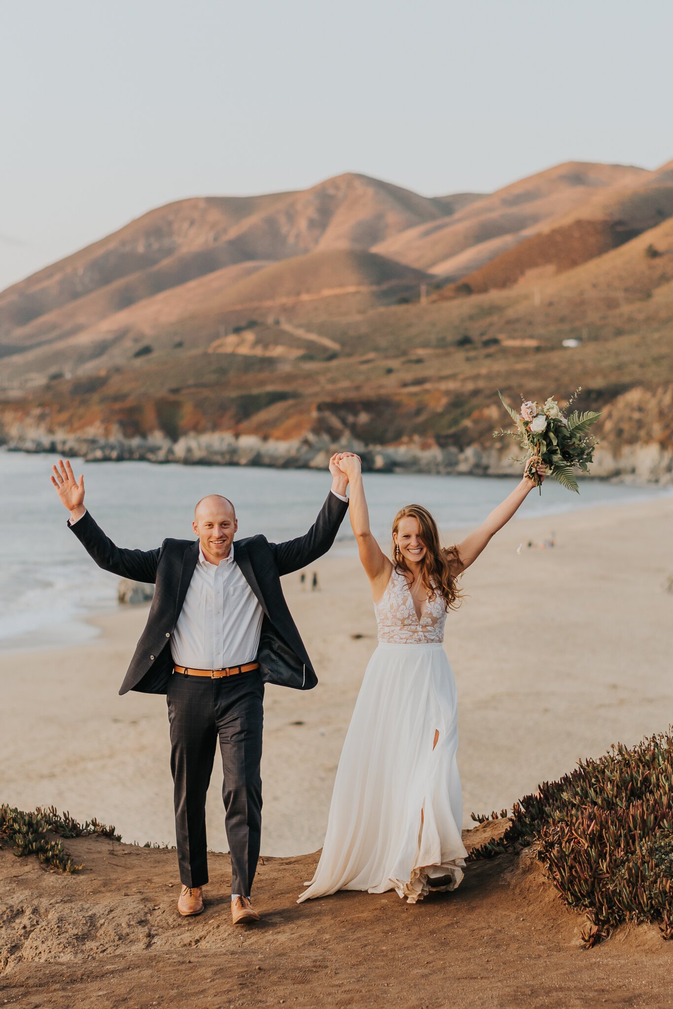 Big Sur Elopement Bride and groom in wedding attire with both arms in air celebrating