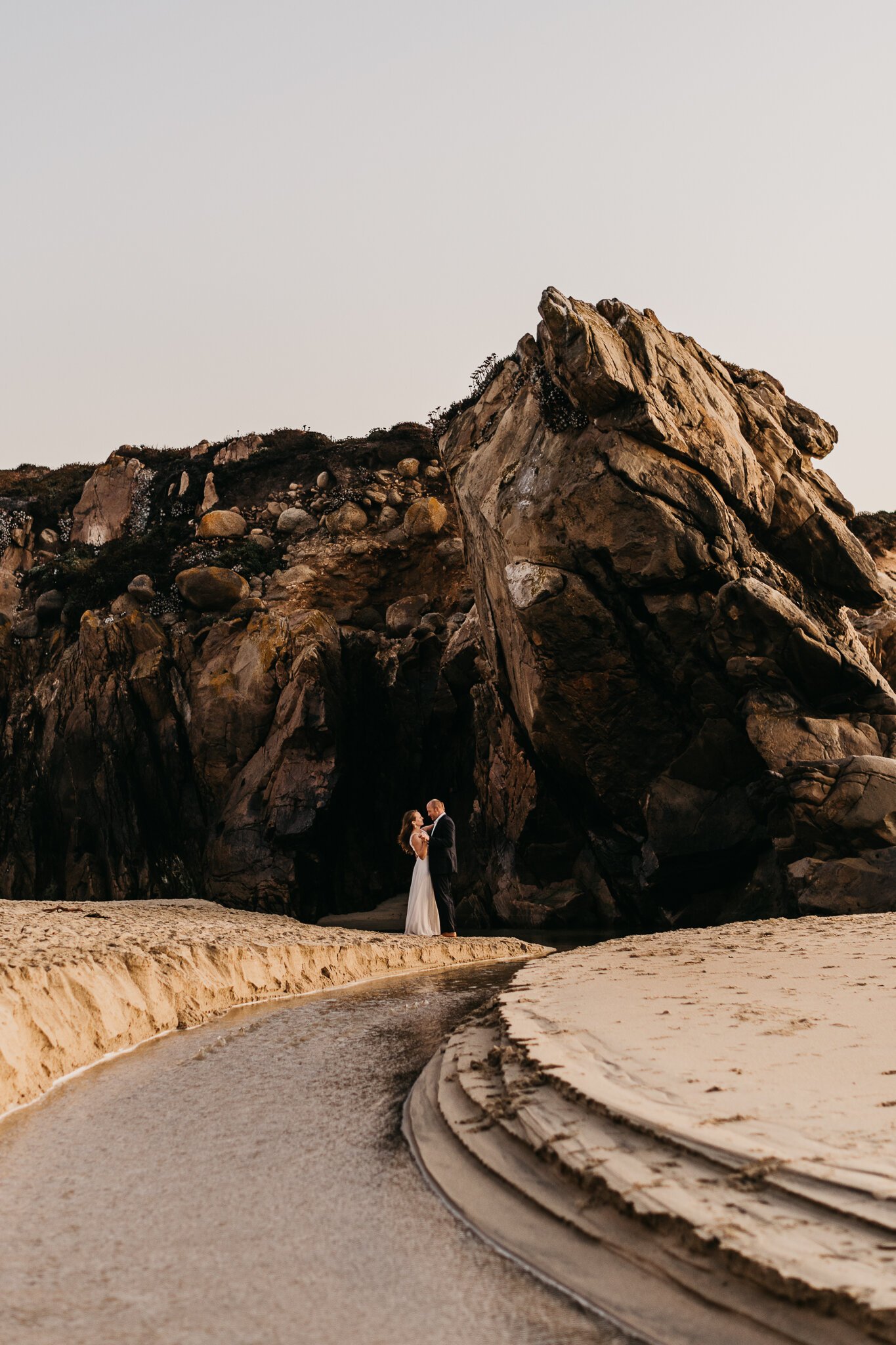 Ventana Fall elopement, bride and groom on the beach dancing by a small stream with cliffs in background