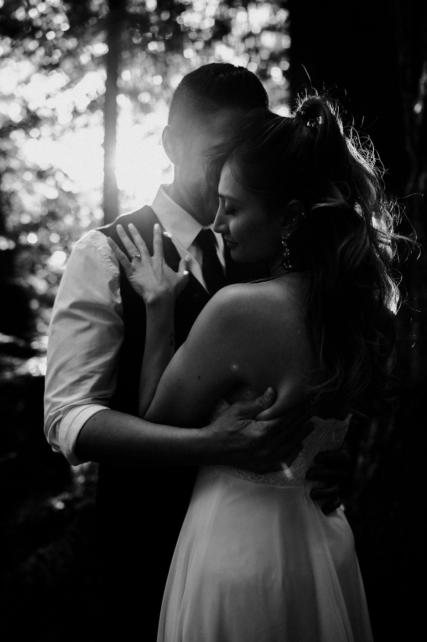 black and white photo of Couple in tall redwoods embracing with sunlight shining through trees Big Sur couples photo session