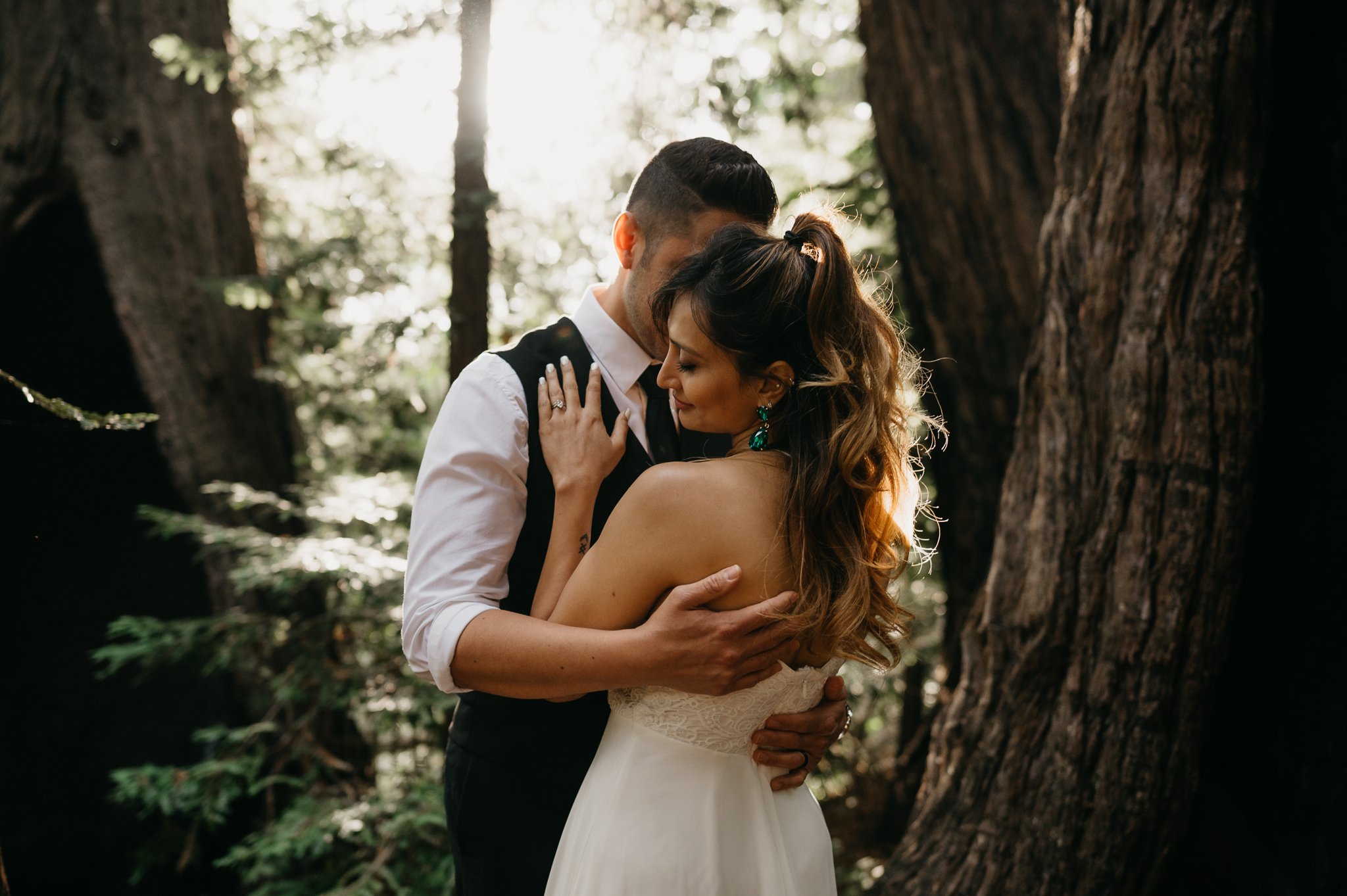 couple dressed in wedding attire in redwoods hugging with sunlight shining through trees in Big Sur California