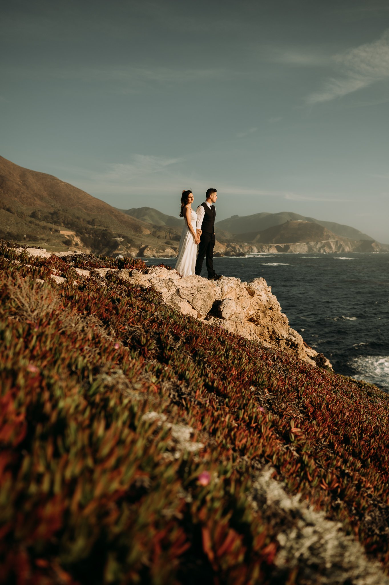 Couple dressed in wedding attire on cliffs to pose for photo Big Sur
