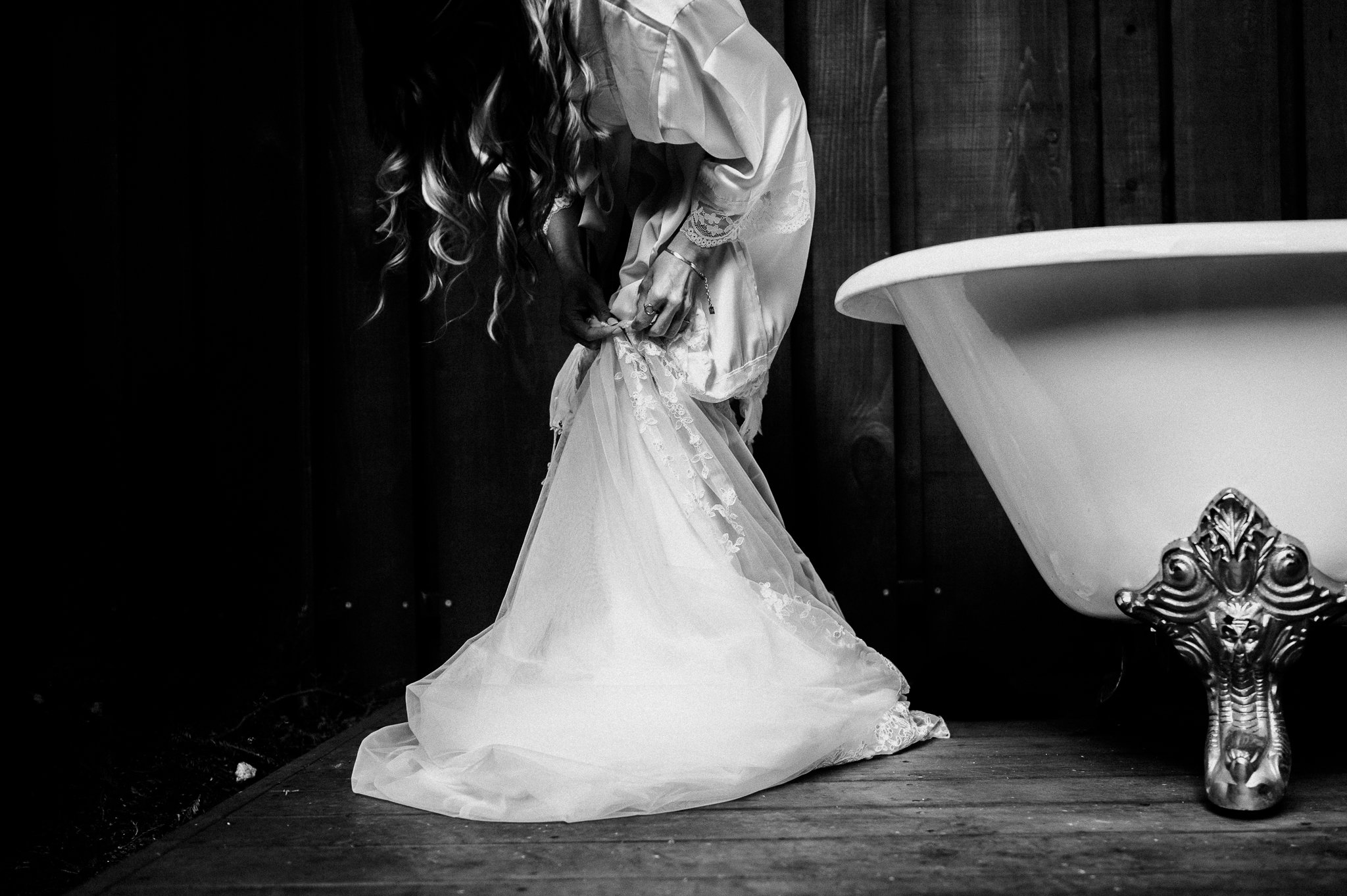 black and white photo of bride adjusting dress beside an old claw foot tub