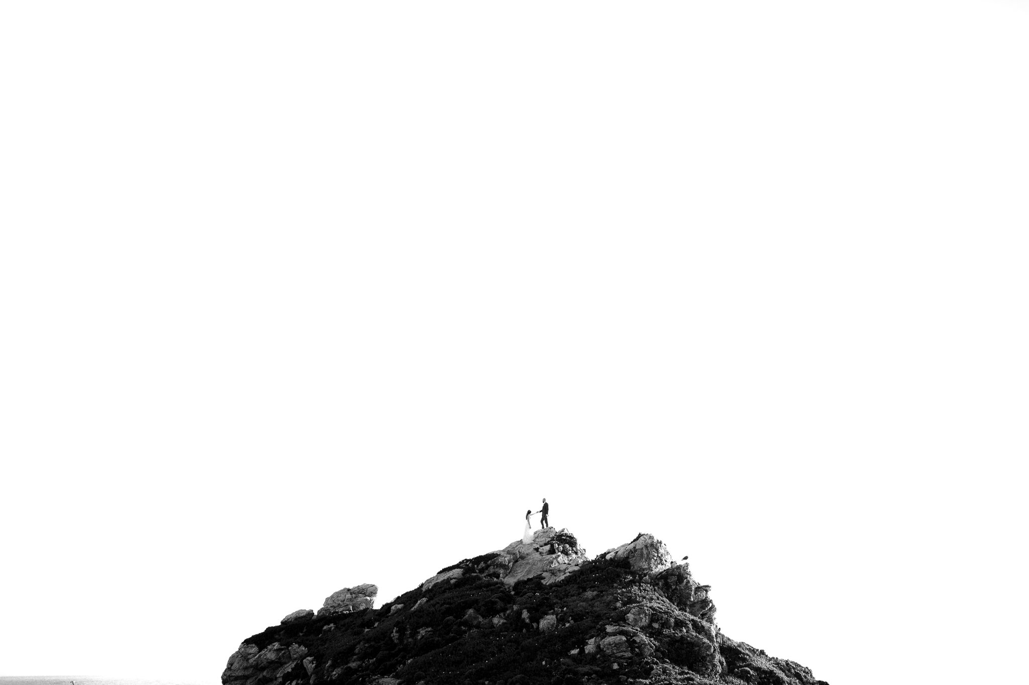 Black and white photo with bride and groom posing on top of a cliff in Big Sur