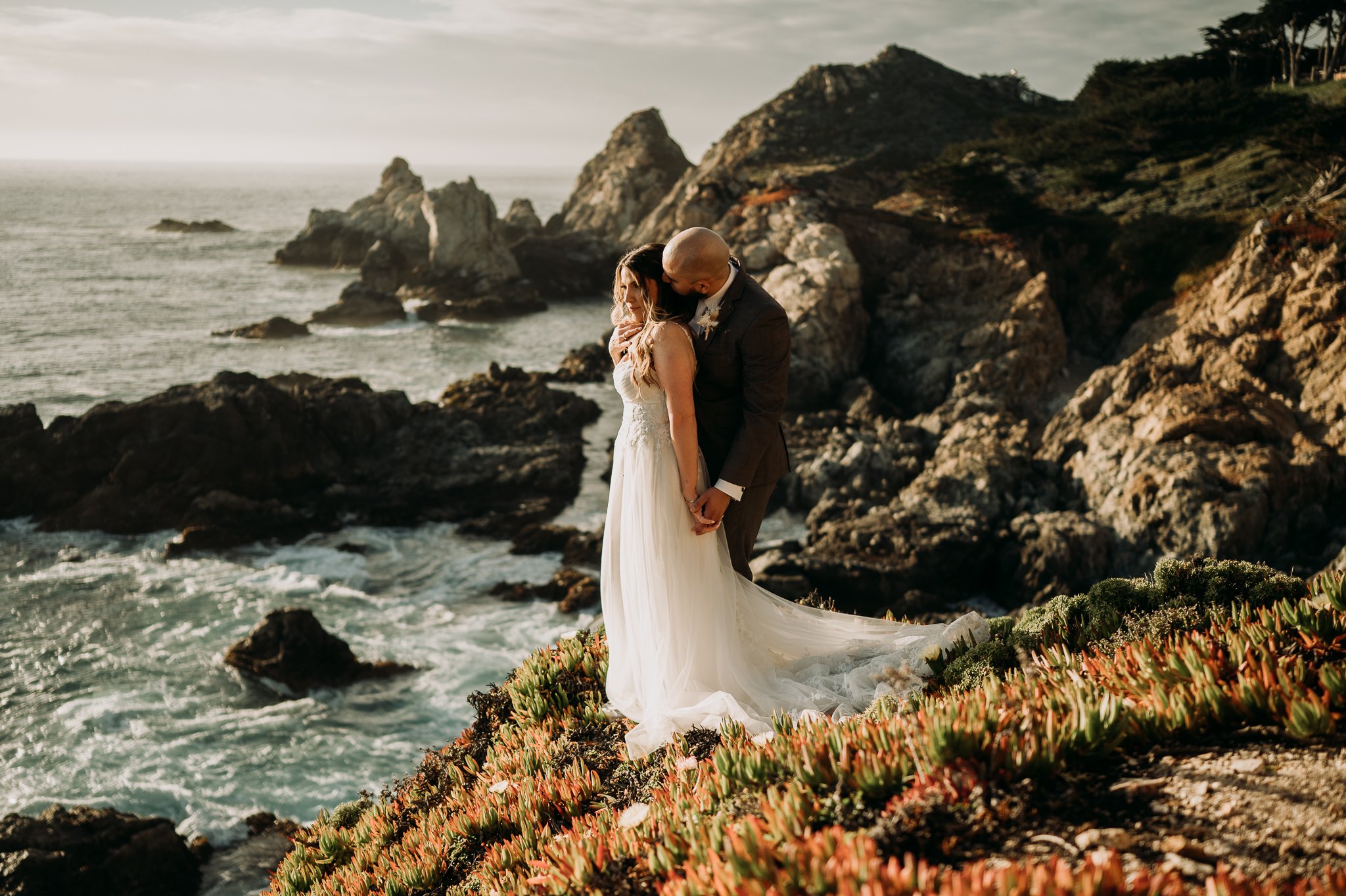 newly married couple posing on path by the cliffs at Big Sur in bridal dress and suit