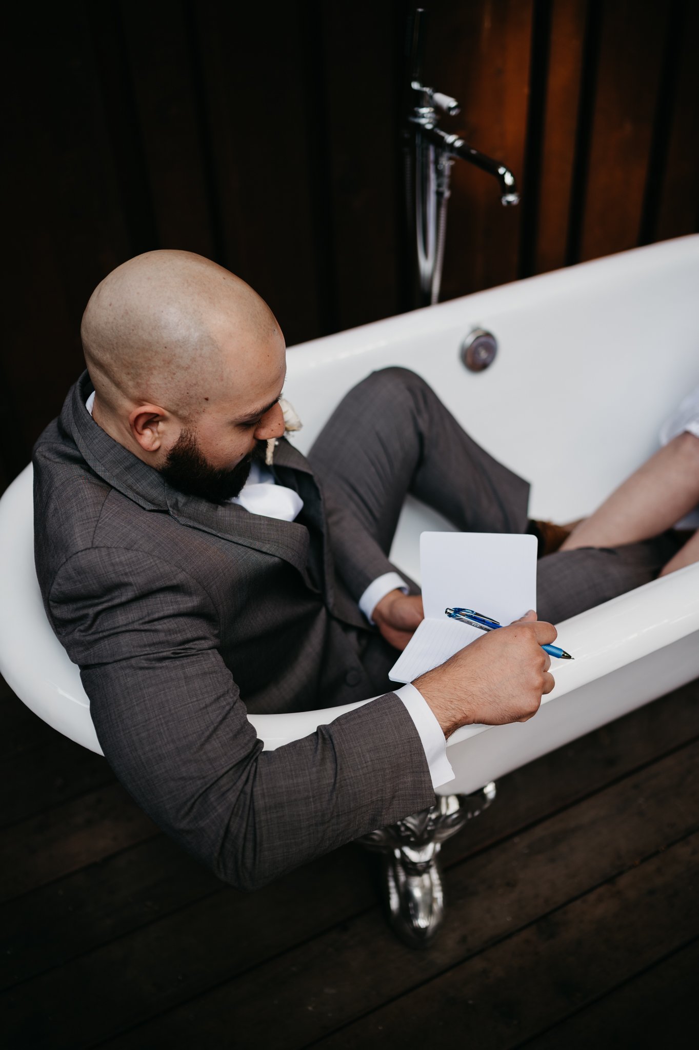 Groom sitting in claw foot tub writing wedding vows in grey suit before elopement at Glen Oaks Big Sur