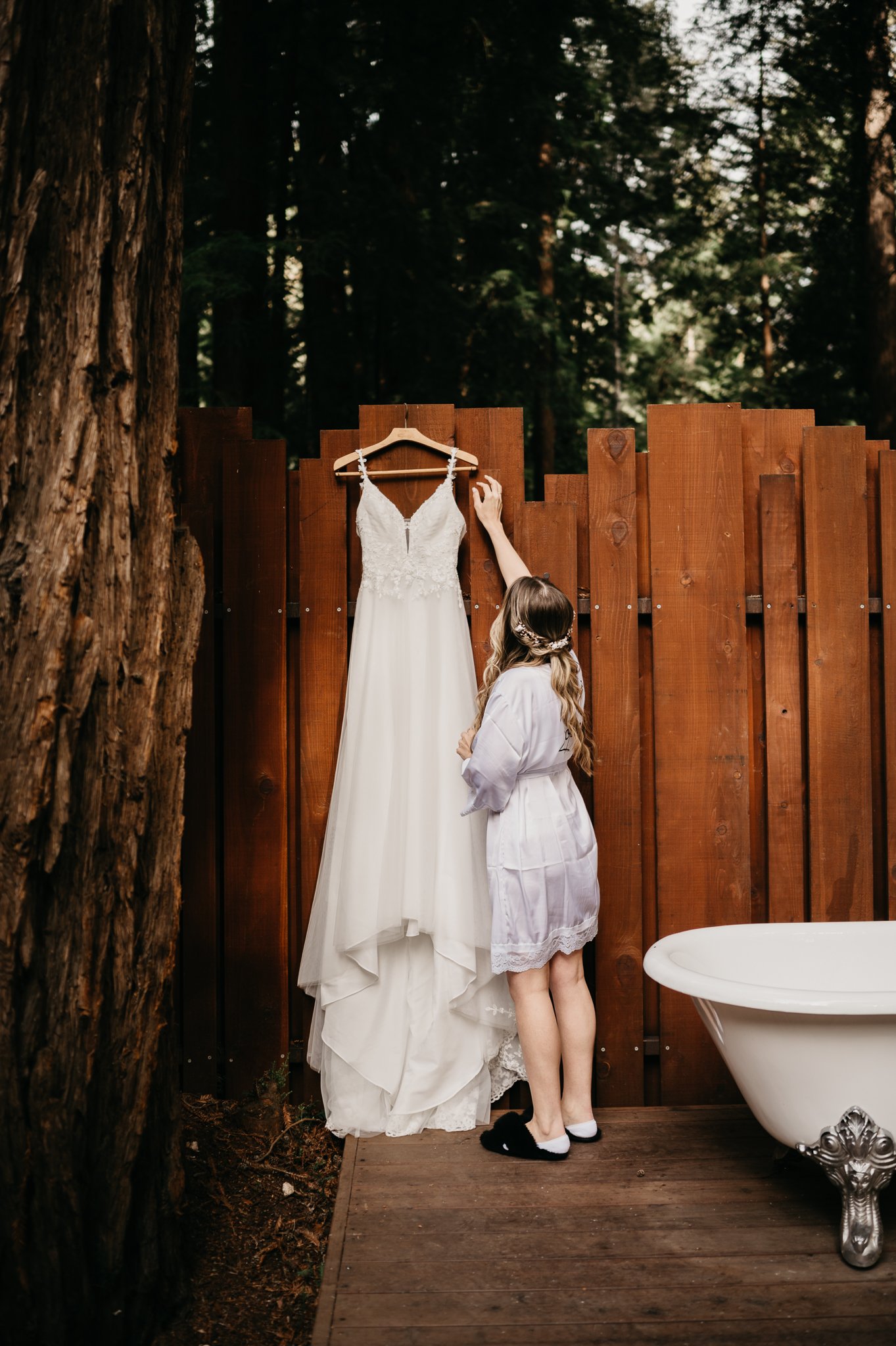 Bridal gown hanging on fence with bride reaching up to take dress down at Glen Oaks Big Sur