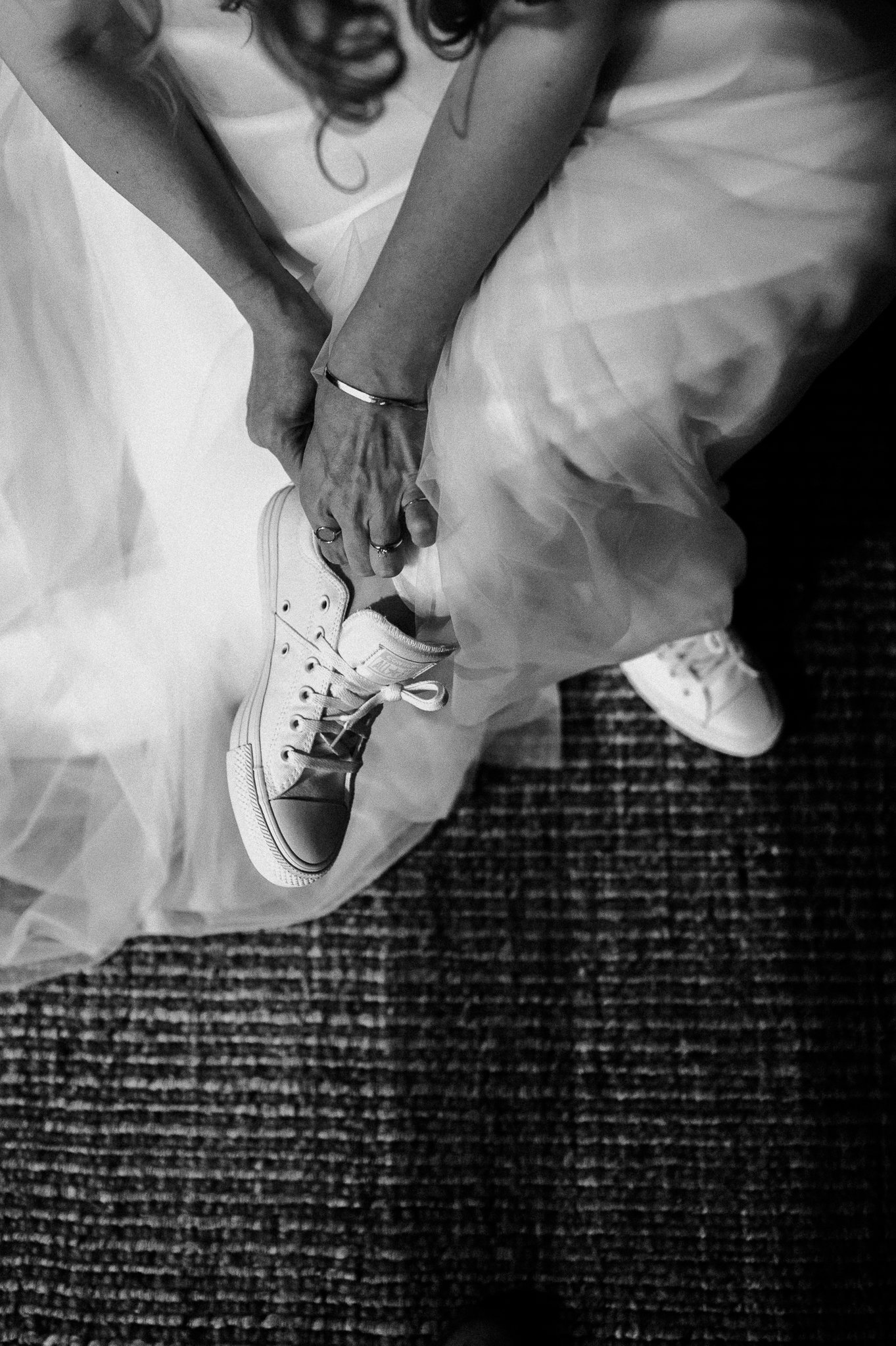 Black and white photo of bride putting on white tennis shoes before adventure elopement in the redwoods at Big Sur