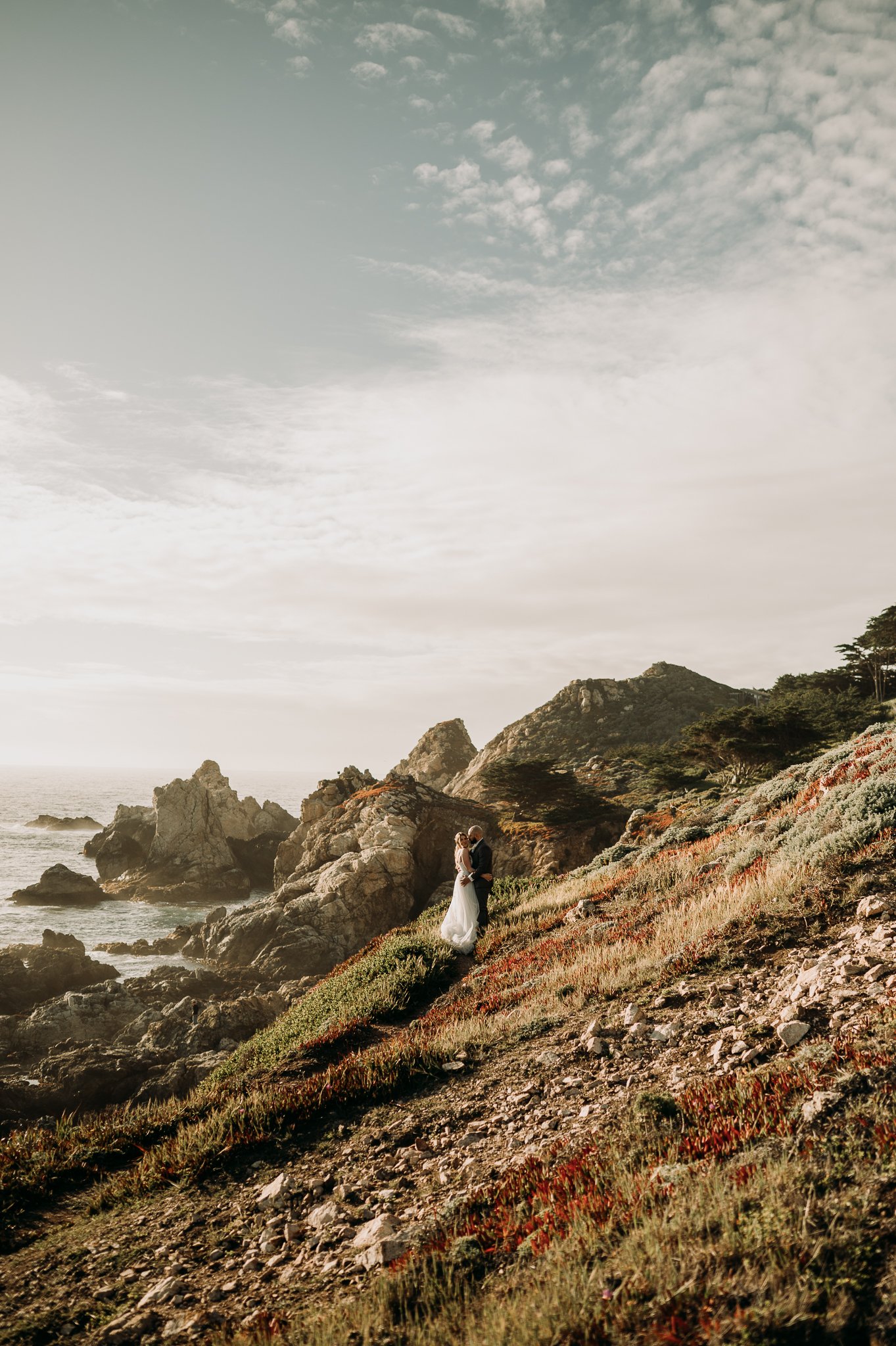 Elopement couple on the cliffs at Big Sur in wedding attire with cliffs and pacific ocean in background