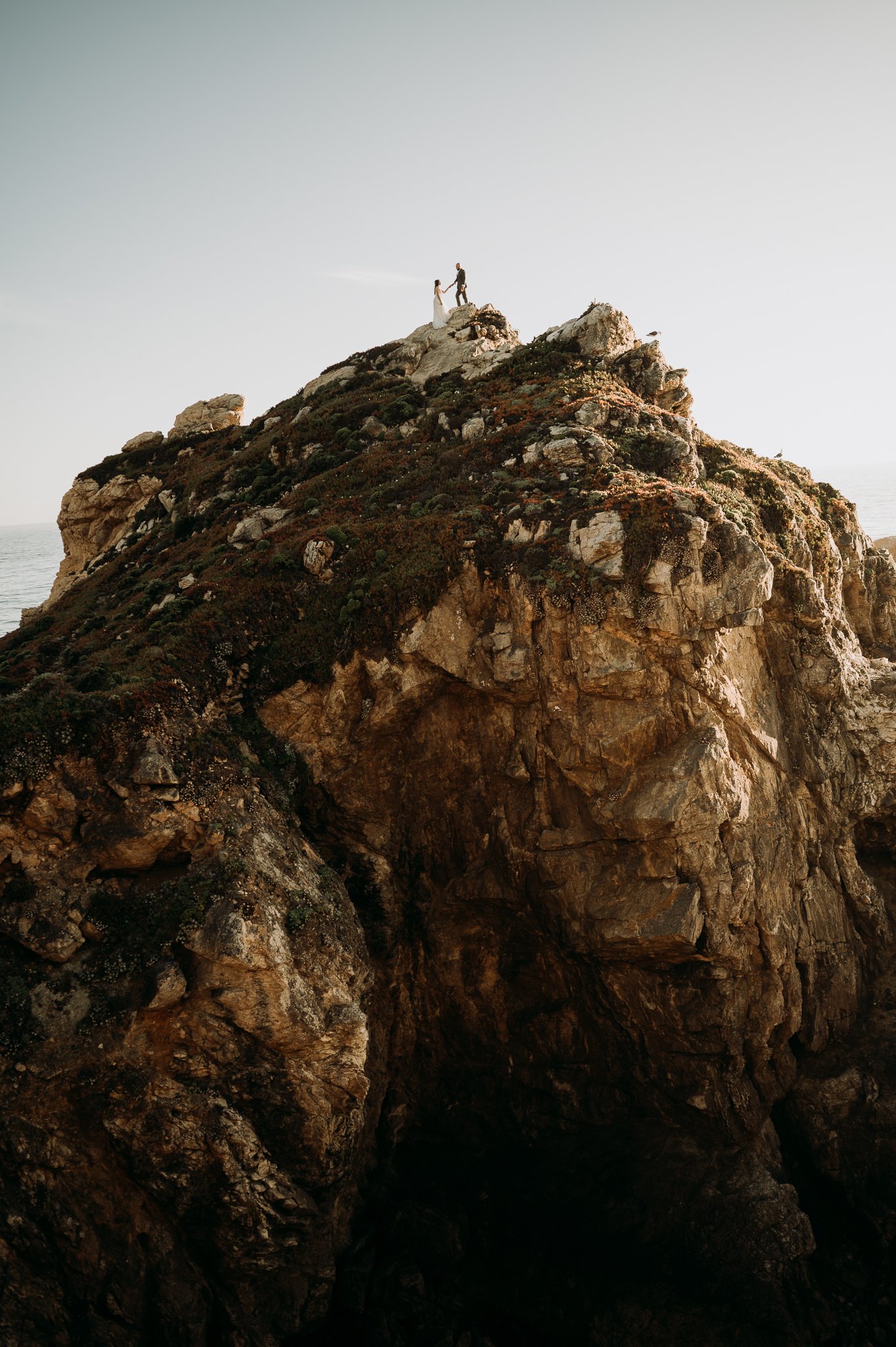 elopement couple high on cliff overlooking the Pacific Ocean at Big Sur