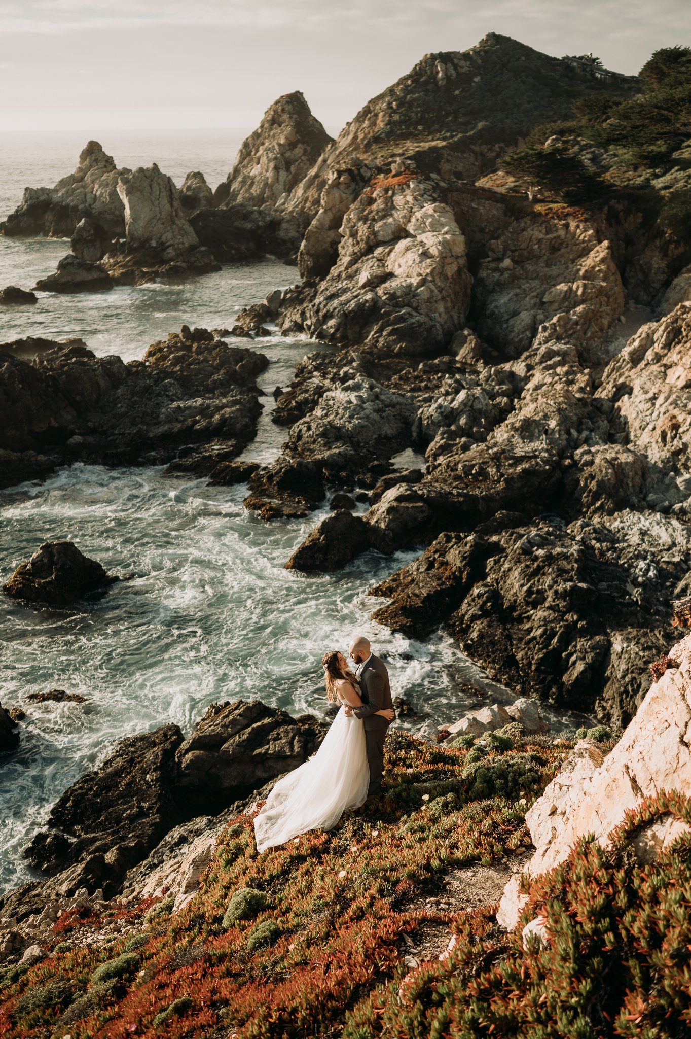 elopement couple in bridal attire embracing on path overlooking the Pacific Ocean at Big Sur