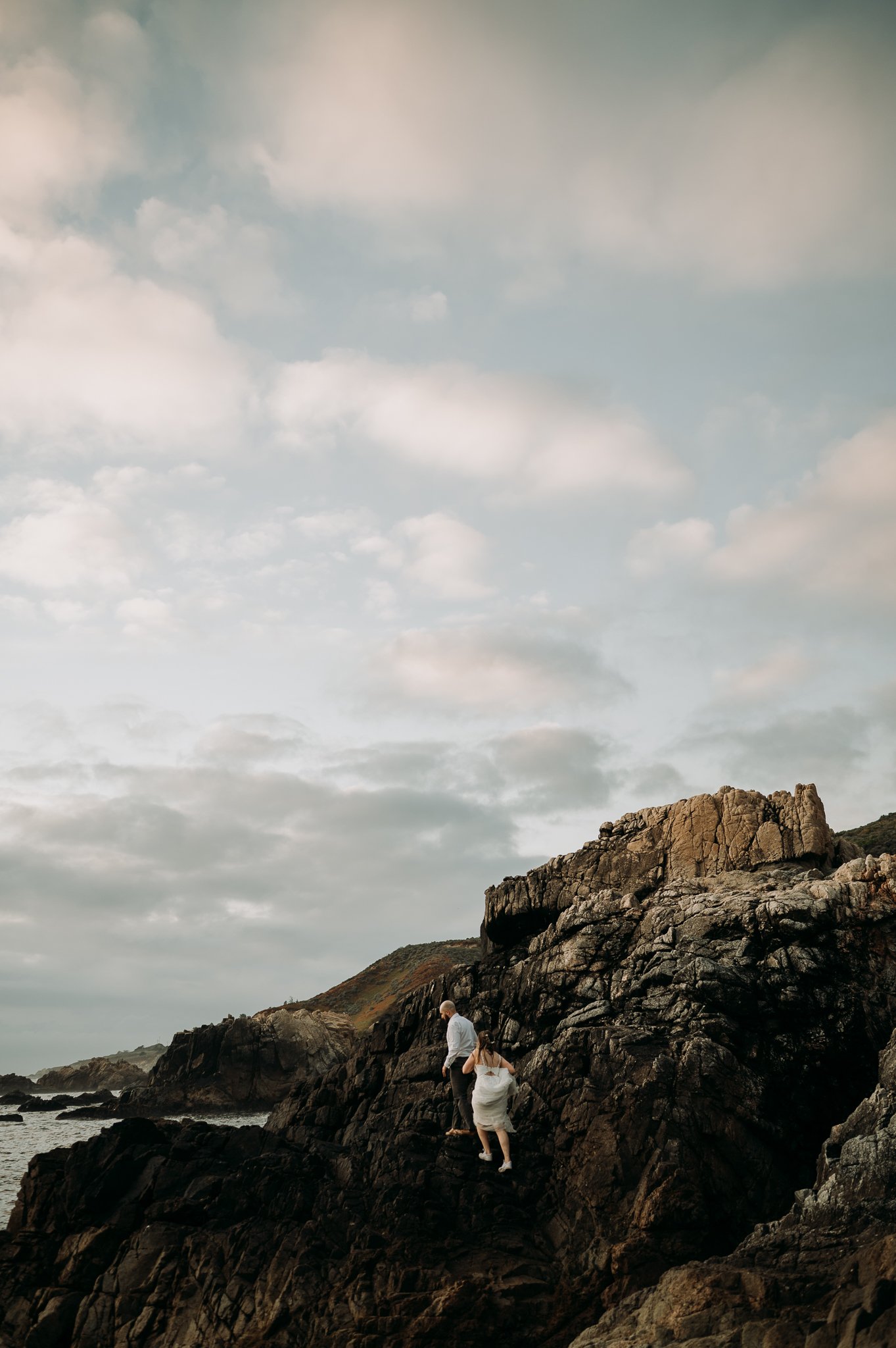 newly married couple in bridal dress and suit climbing cliffs at Big Sur California 
