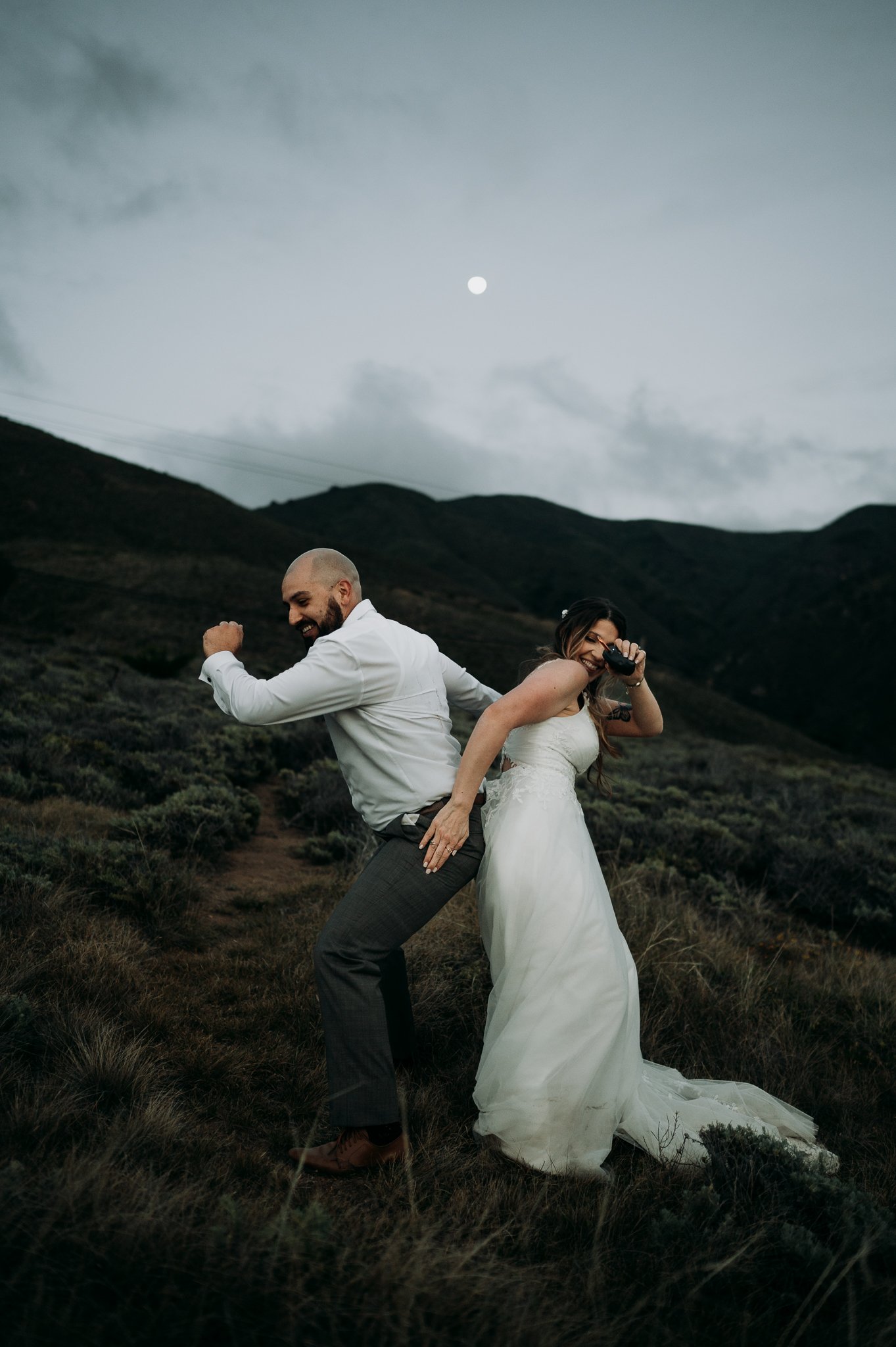 Newly married couple in wedding attire dancing on cliff in Big Sur California