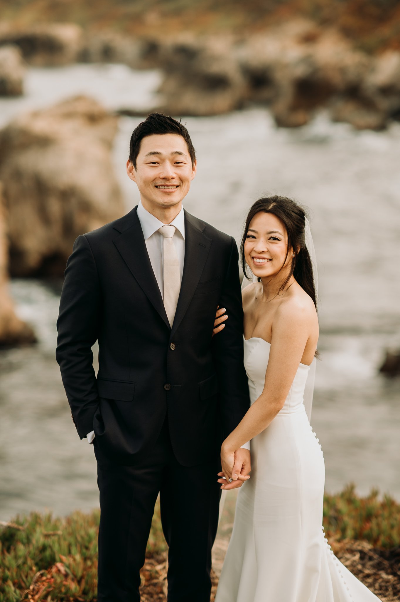bride and groom standing side by side above Pacific Ocean in wedding attire 