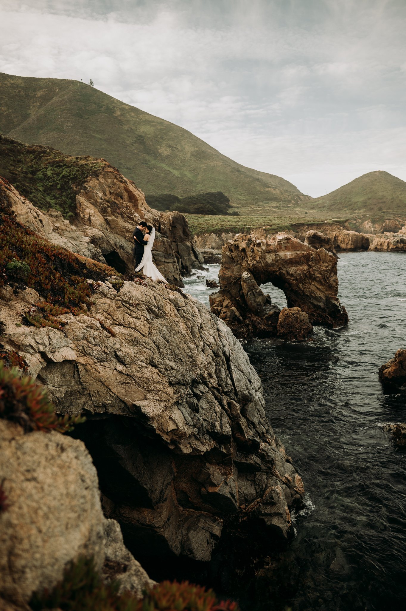 Elopement couple embracing cliffside Big Sur with key hole rock in background