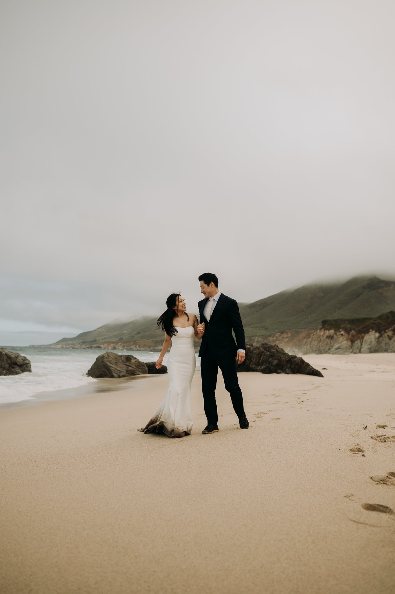 elopement couple in wedding attire walking on beach hand in hand on beach in Big Sur California
