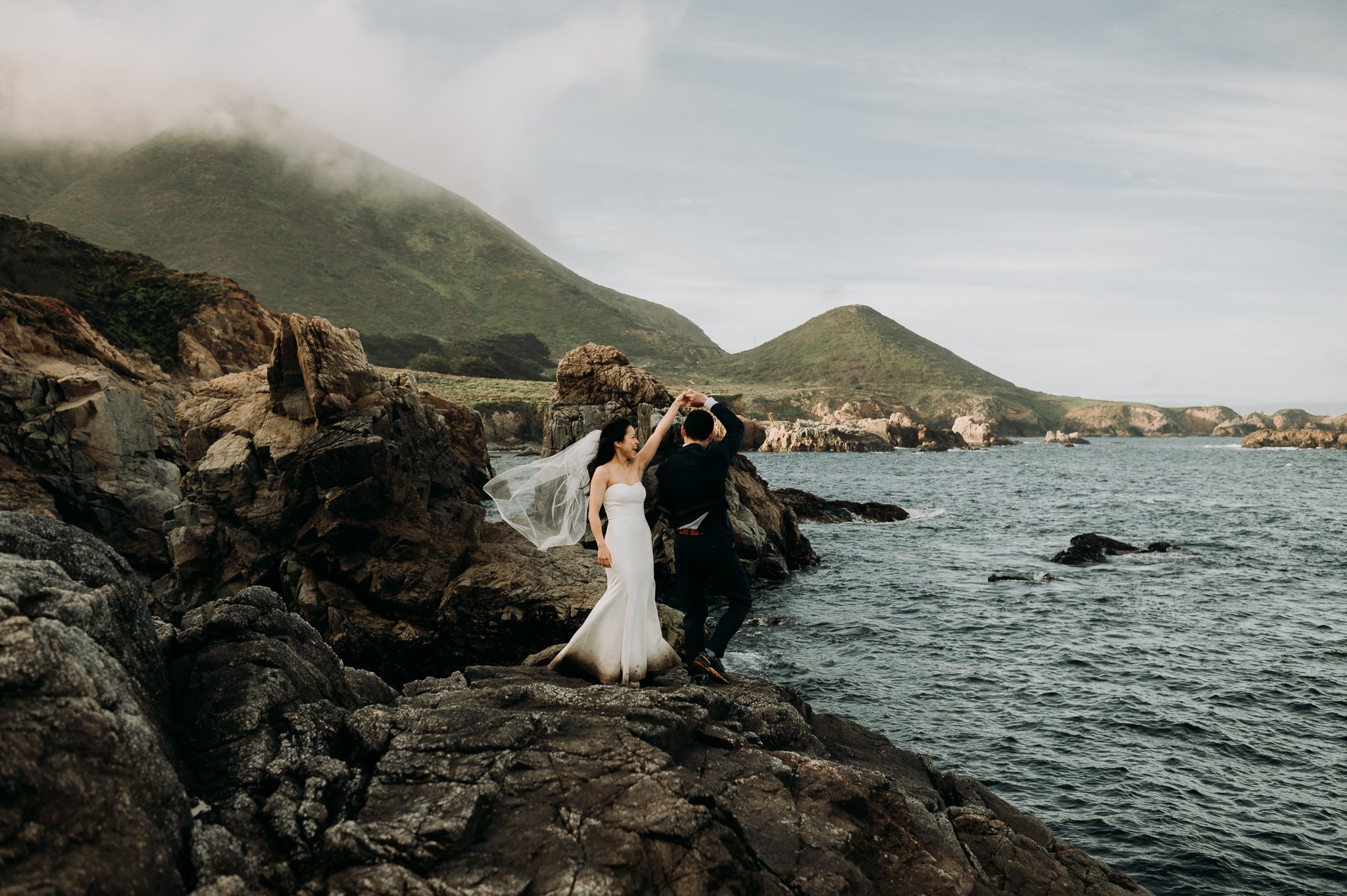 Elopement couple in wedding attire dancing on cliff in Big Sur California