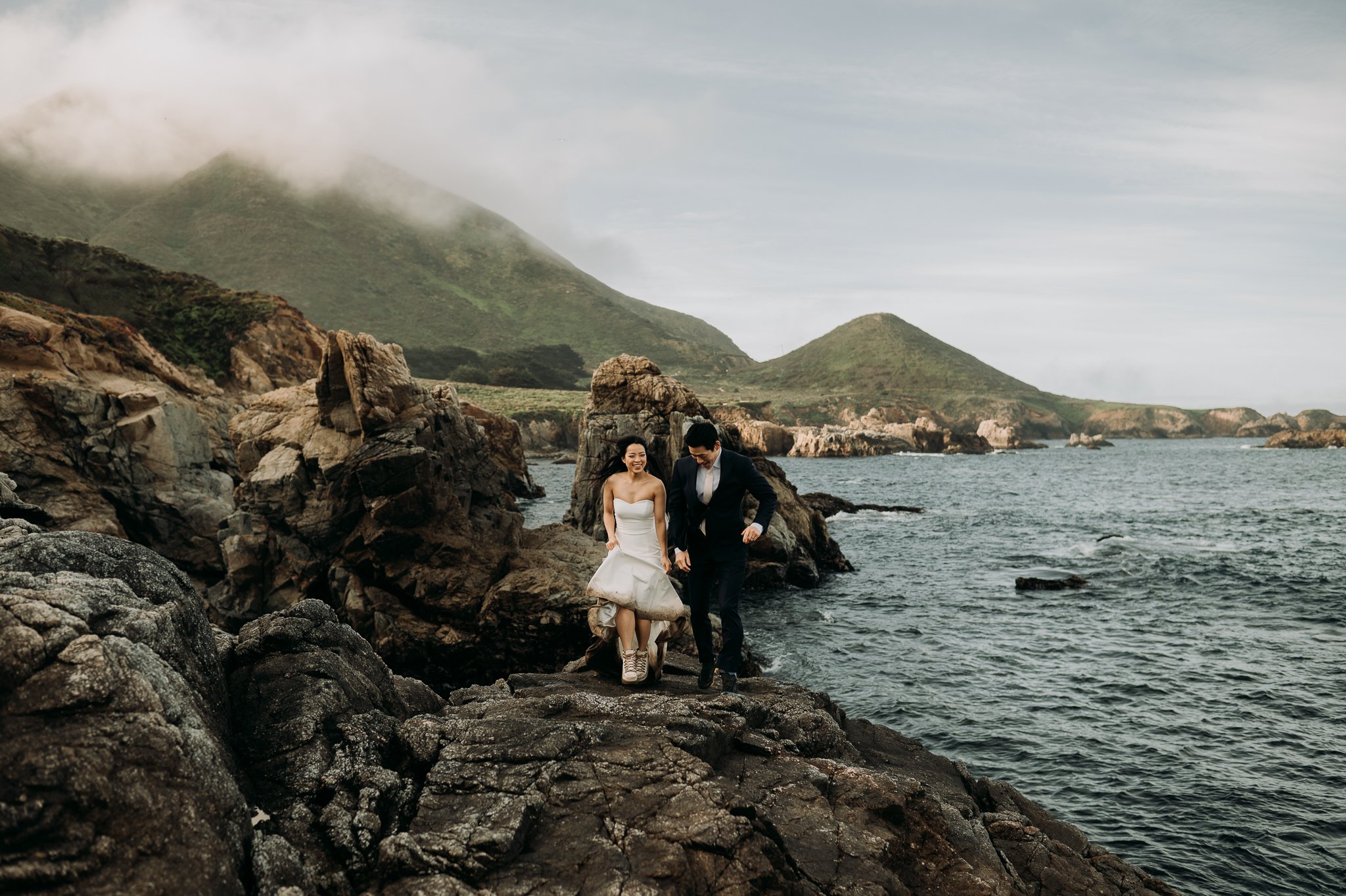 Elopement couple in wedding attire dancing on cliff in Big Sur California