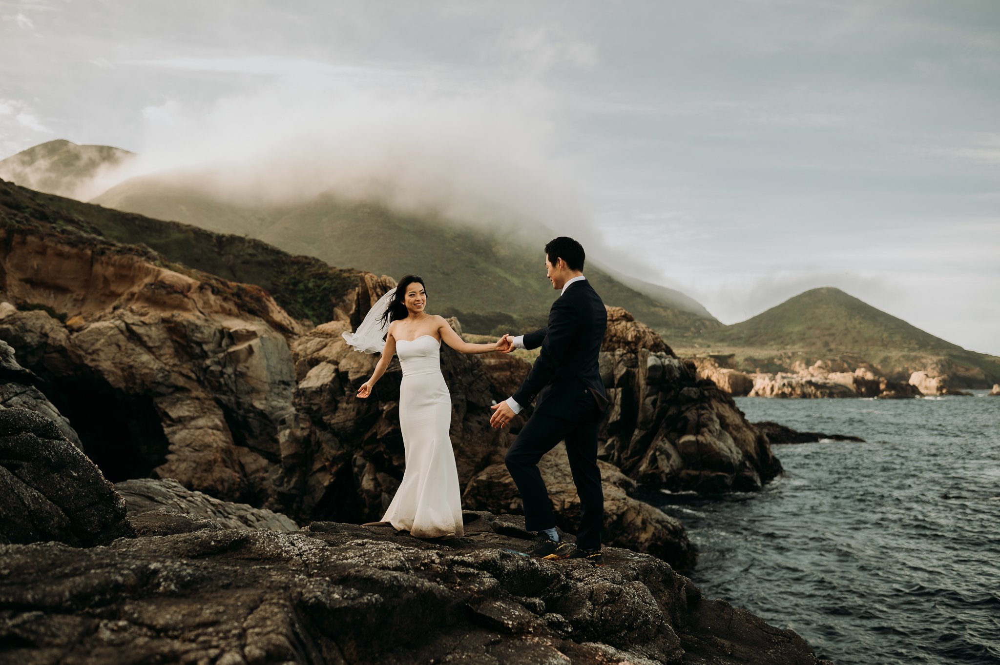 Elopement couple in wedding attire dancing on cliff in Big Sur California