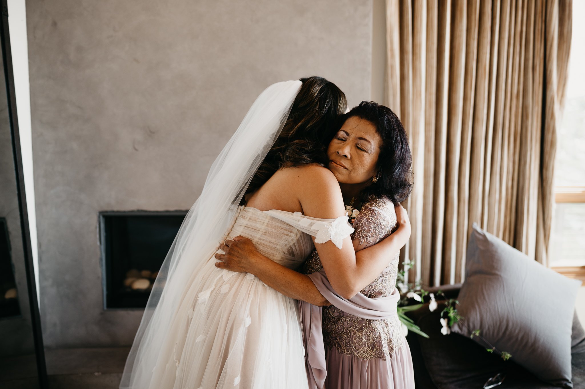 Bride in wedding dress hugging her Mother before ceremony in private room at Wind and Sea Big Sur