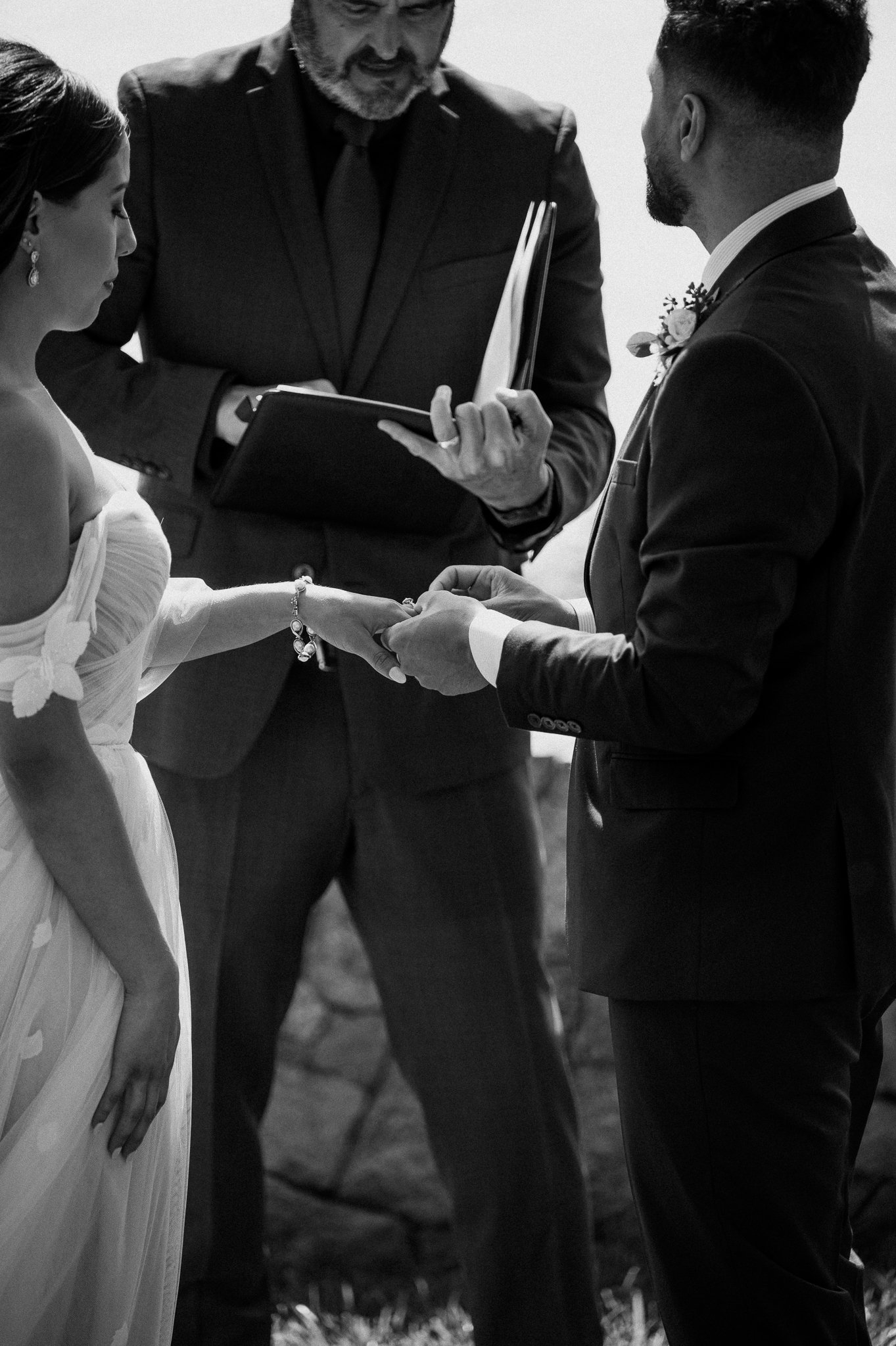 Black and white photo of groom putting ring on brides finger during ceremony