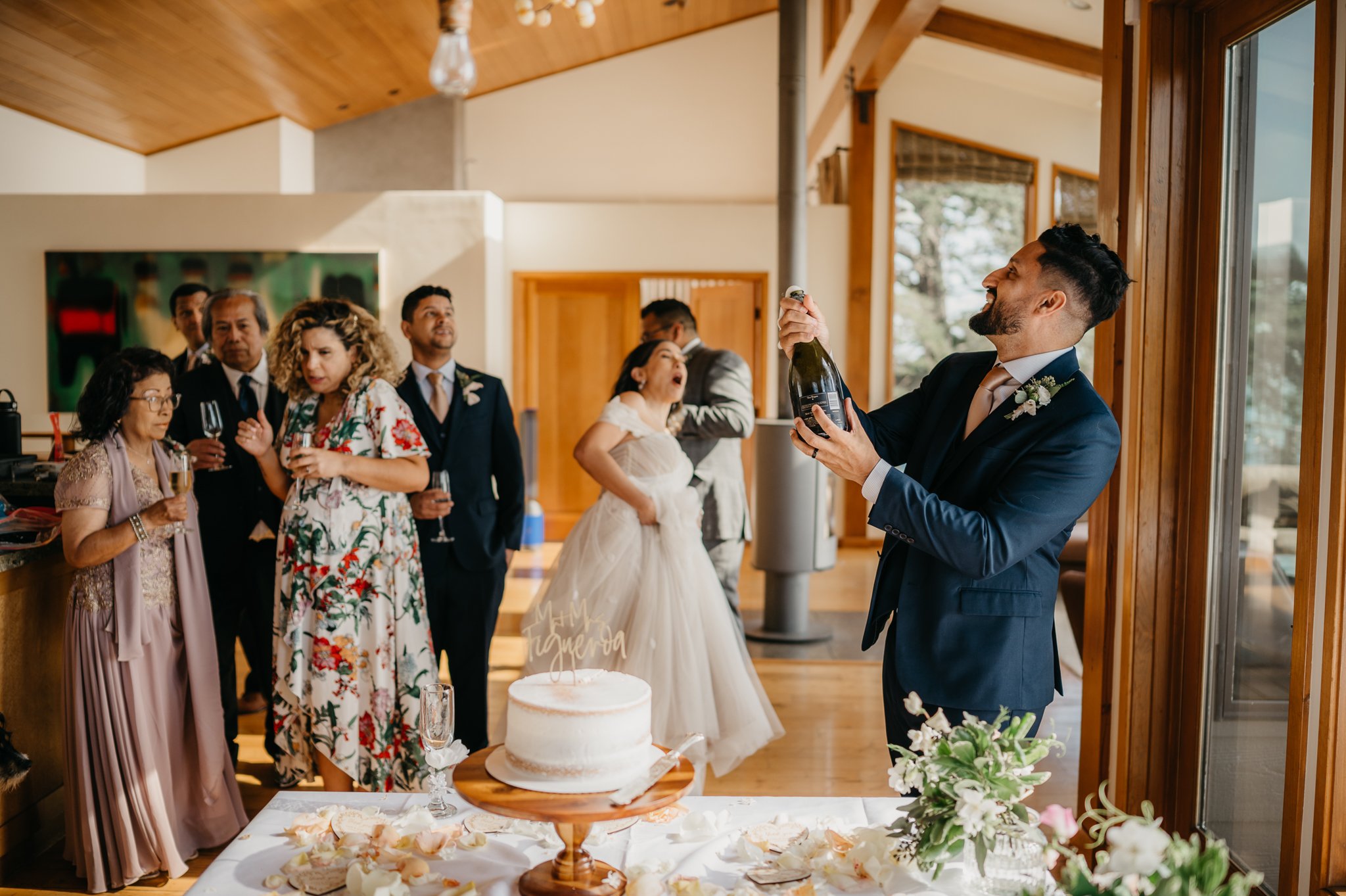 Groom popping champagne with bride and guests 